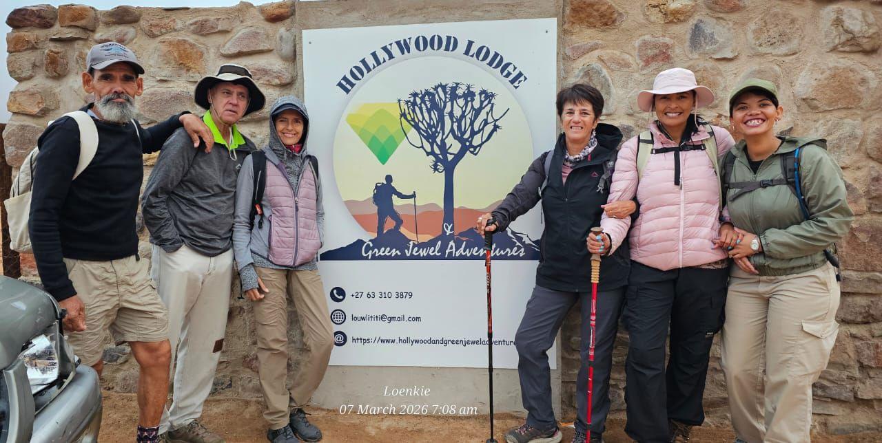 A group of hikers with walking poles poses in front of the Hollywood Lodge and Green Jewel Adventures sign in Namaqualand