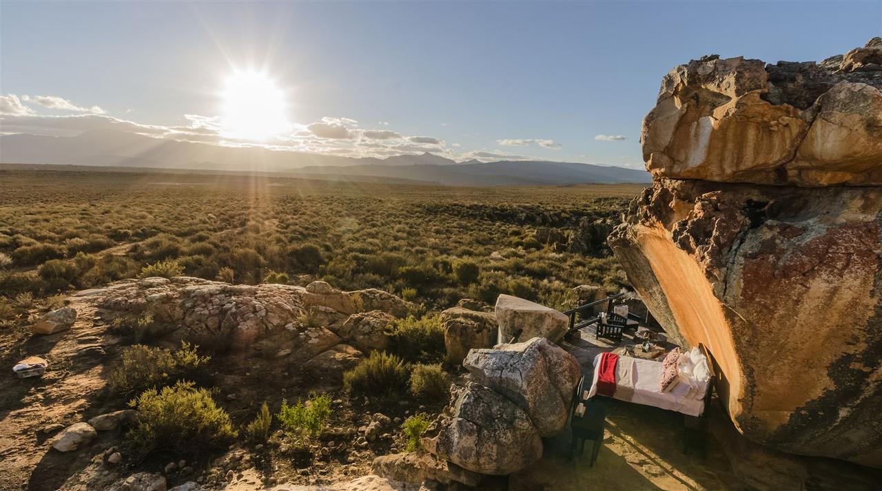An open-air bed under a sandstone rock overhang at Kagga Kamma in the Cederberg, looking out over the veld to distant mountains
