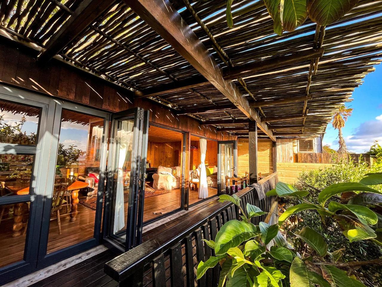 Wooden deck under a reed pergola, with folding doors open to a wood-panelled lounge at Scarborough Nature Lodge