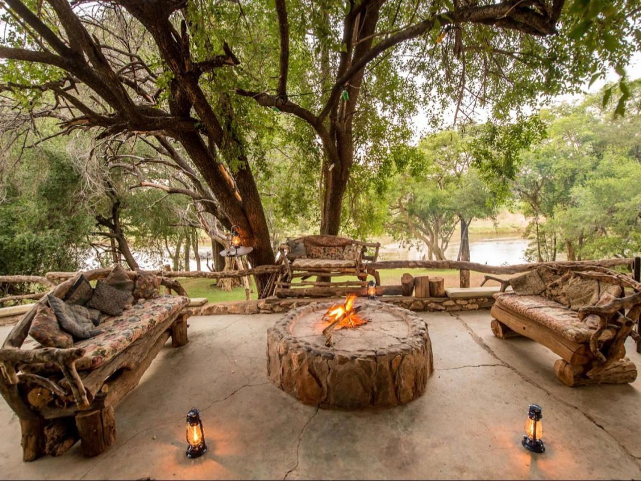 Stone fire pit and rustic wooden benches under trees beside the river at Rio Dos Elefantes River Camp, Greater Kruger