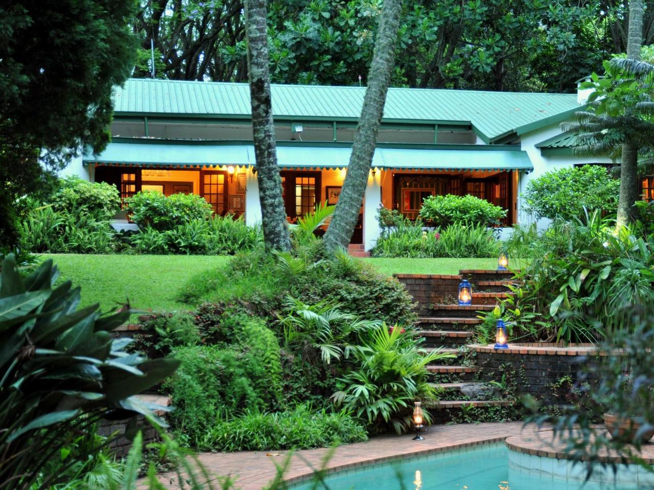 Highgrove House in Hazyview at dusk, with lantern-lit steps leading up through a tropical garden from the pool