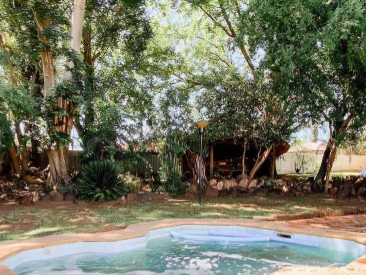 Swimming pool in a shady garden with tall trees and a thatched lapa at De Kaapse Rust Boutique Guesthouse in Parys