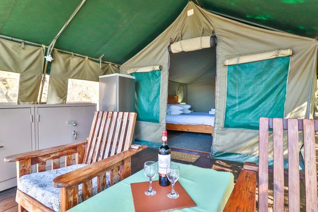 Covered deck of a tented chalet at Valley of the Rainbow near Dullstroom, with wooden chairs, a fridge and the bedroom behind