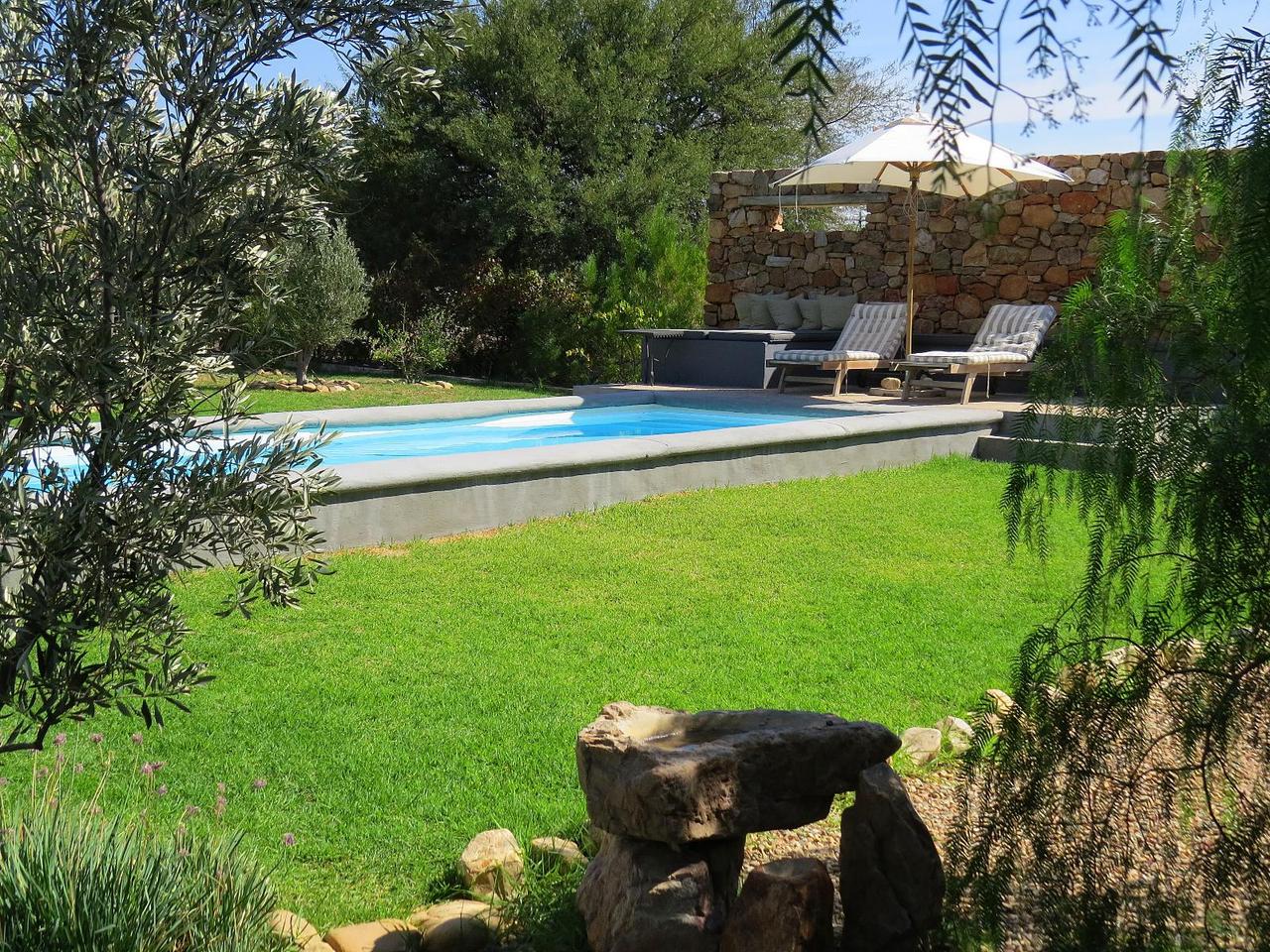 Garden pool with sun loungers and an umbrella beside a stone wall at Olive Grove Cottage and Little Pip in Prince Albert