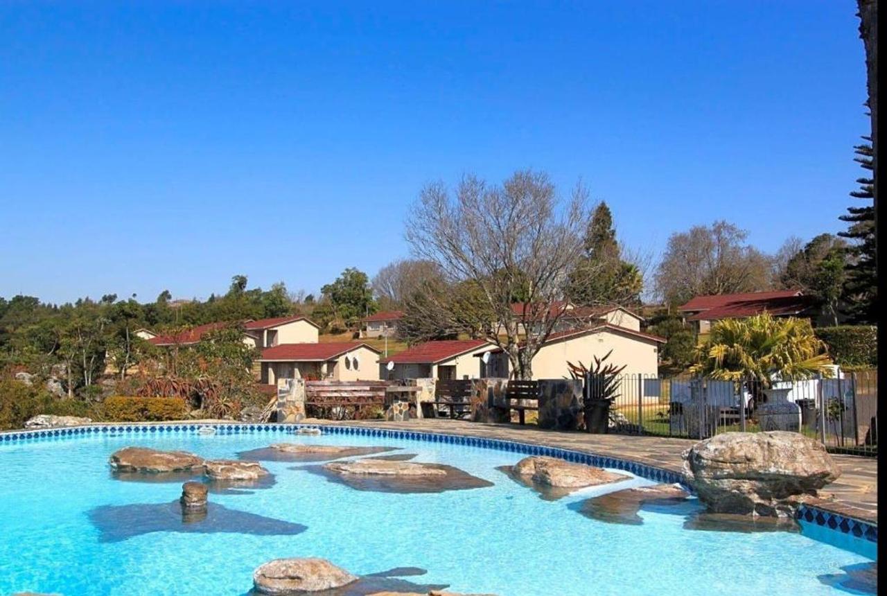 Communal swimming pool with rocks, in front of red-roofed chalets at Panorama Home 19 in Graskop