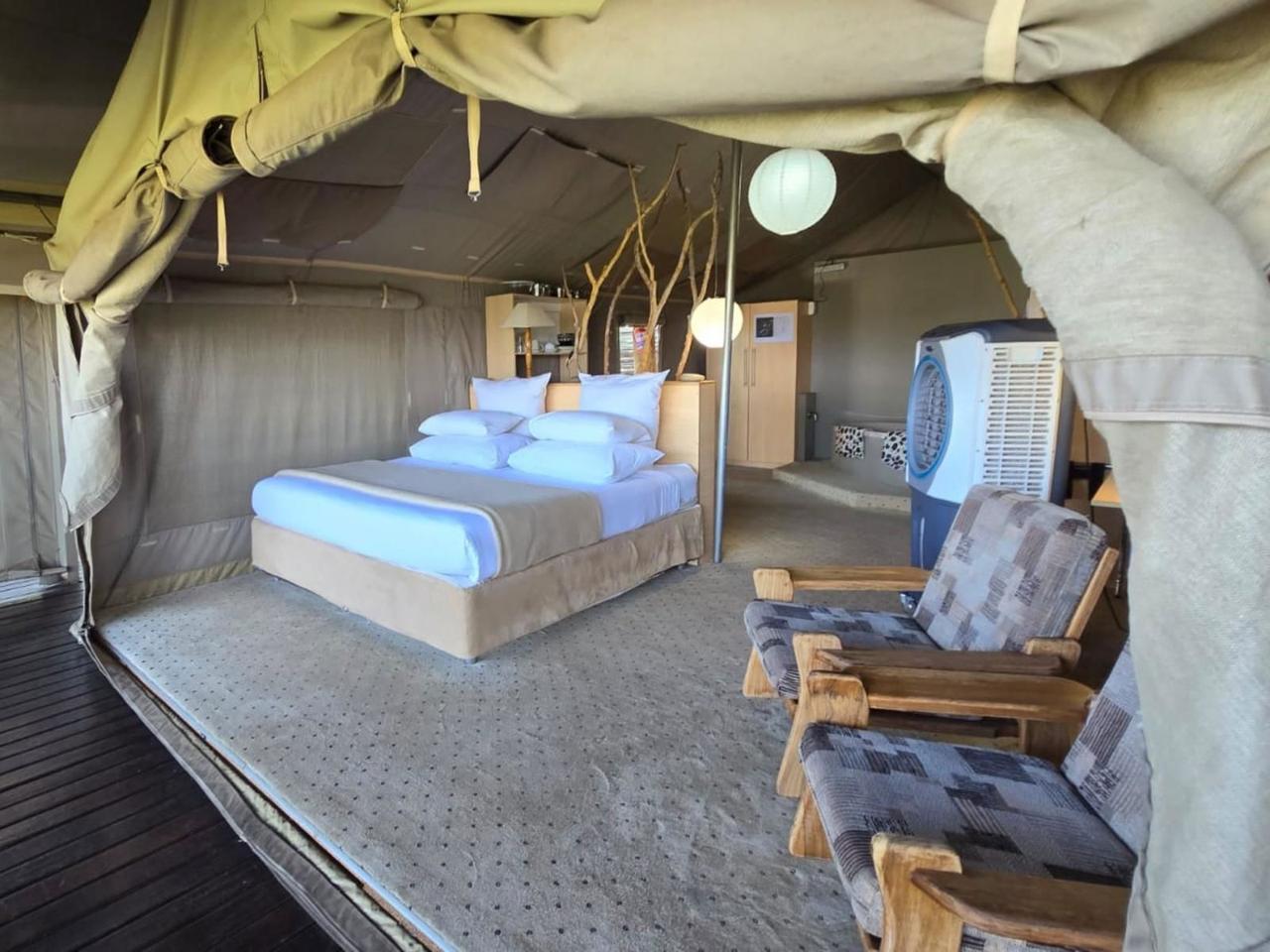 Inside a safari tent at Thulani Game Lodge in the Waterberg, with a large bed, armchairs and canvas walls rolled up