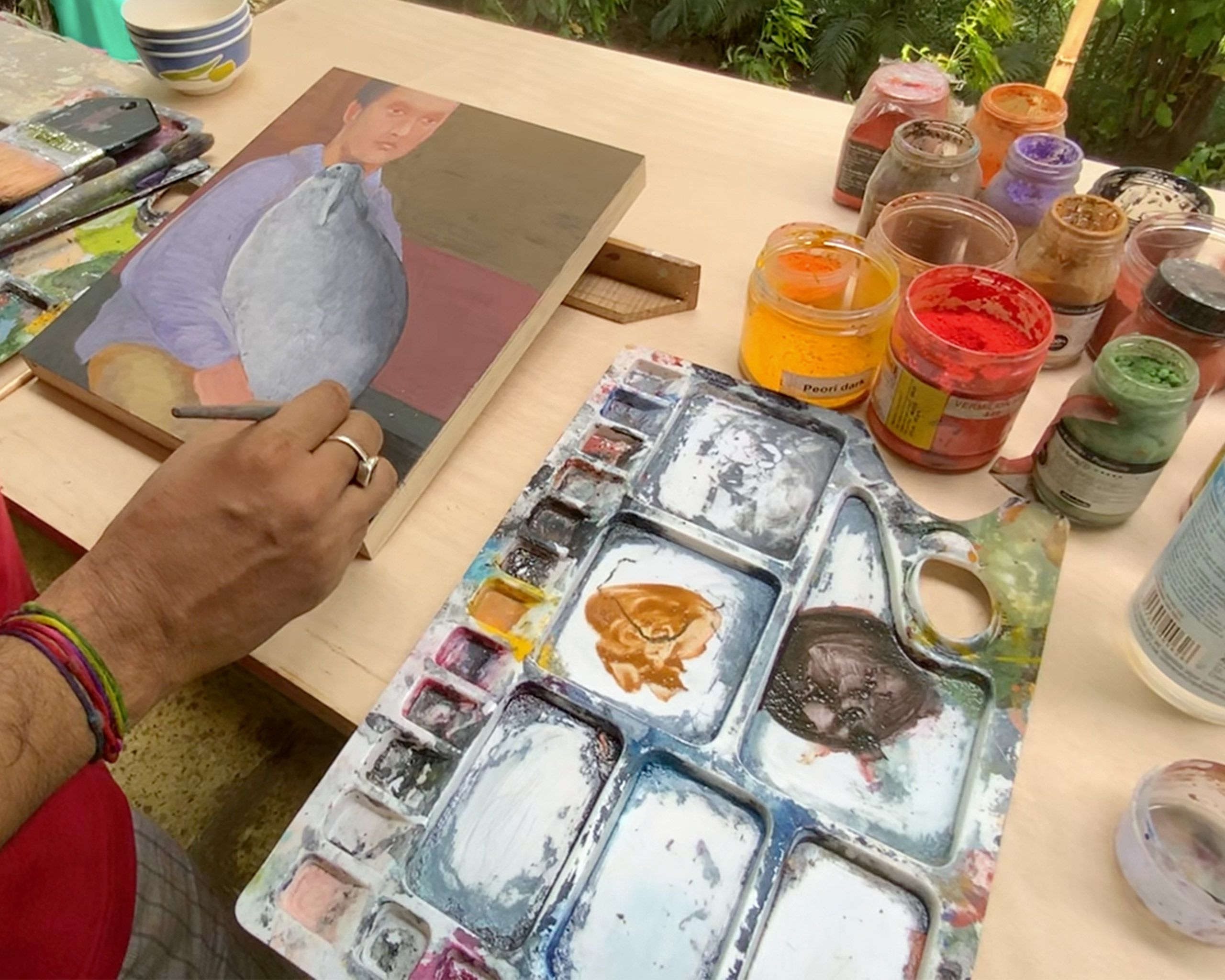 A still from a video by Sashikanth Thavudoz of Baliga working on a painting on a ledge in his studio, dated 2021.