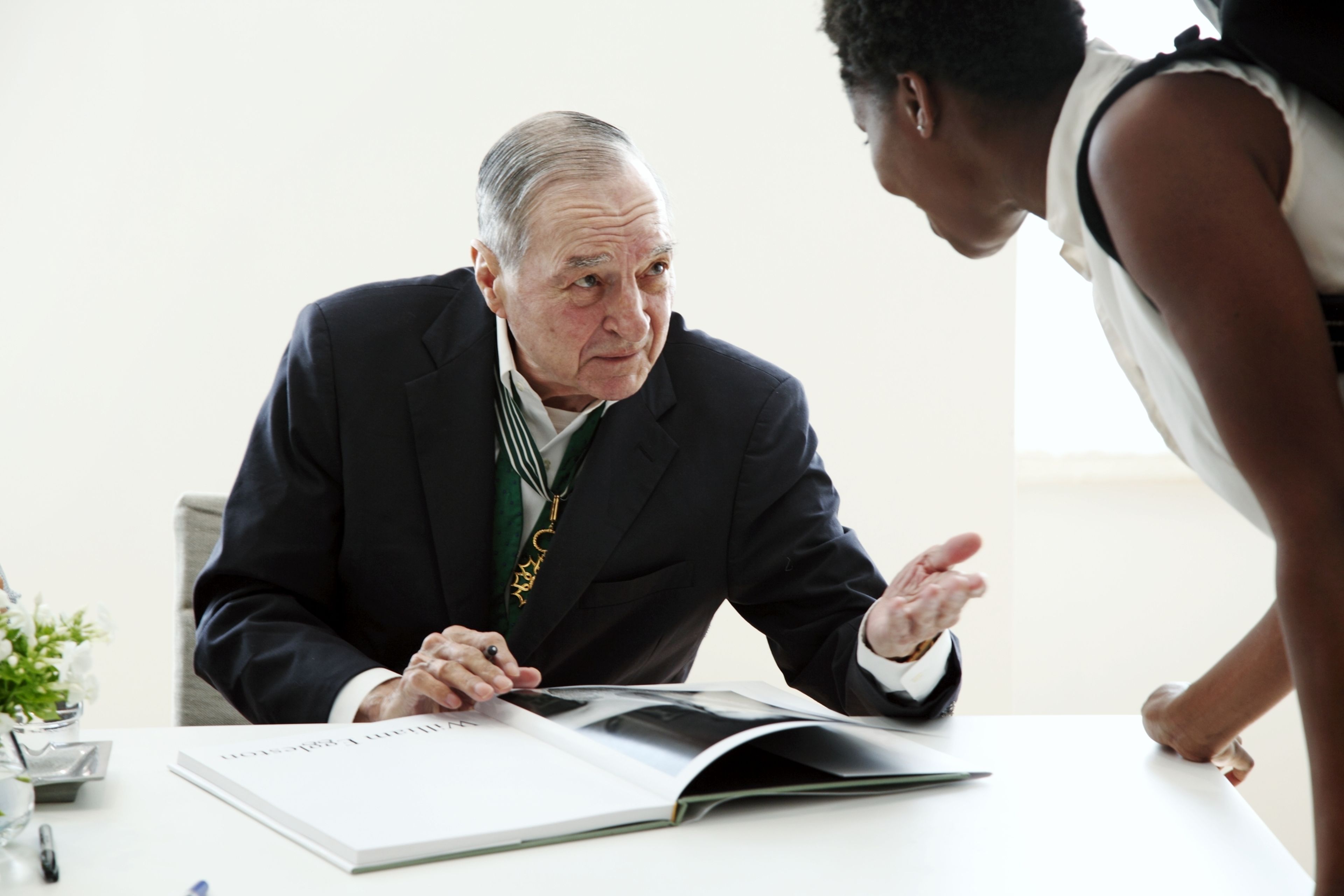 A photograph of William Eggleston signing a book.