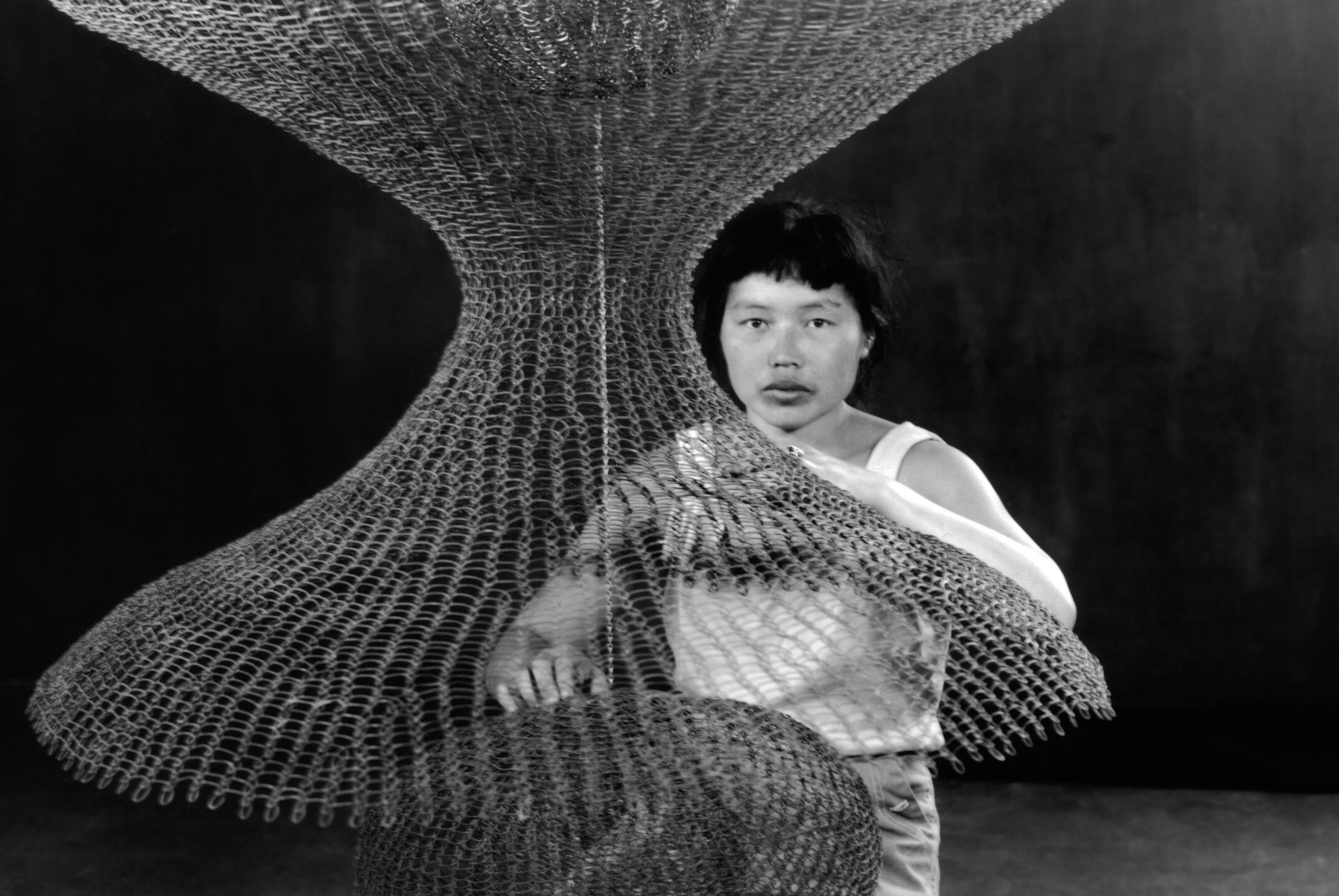 Ruth Asawa kneeling behind a hanging looped-wire sculpture, 1957 (detail). Photo by Imogen Cunningham