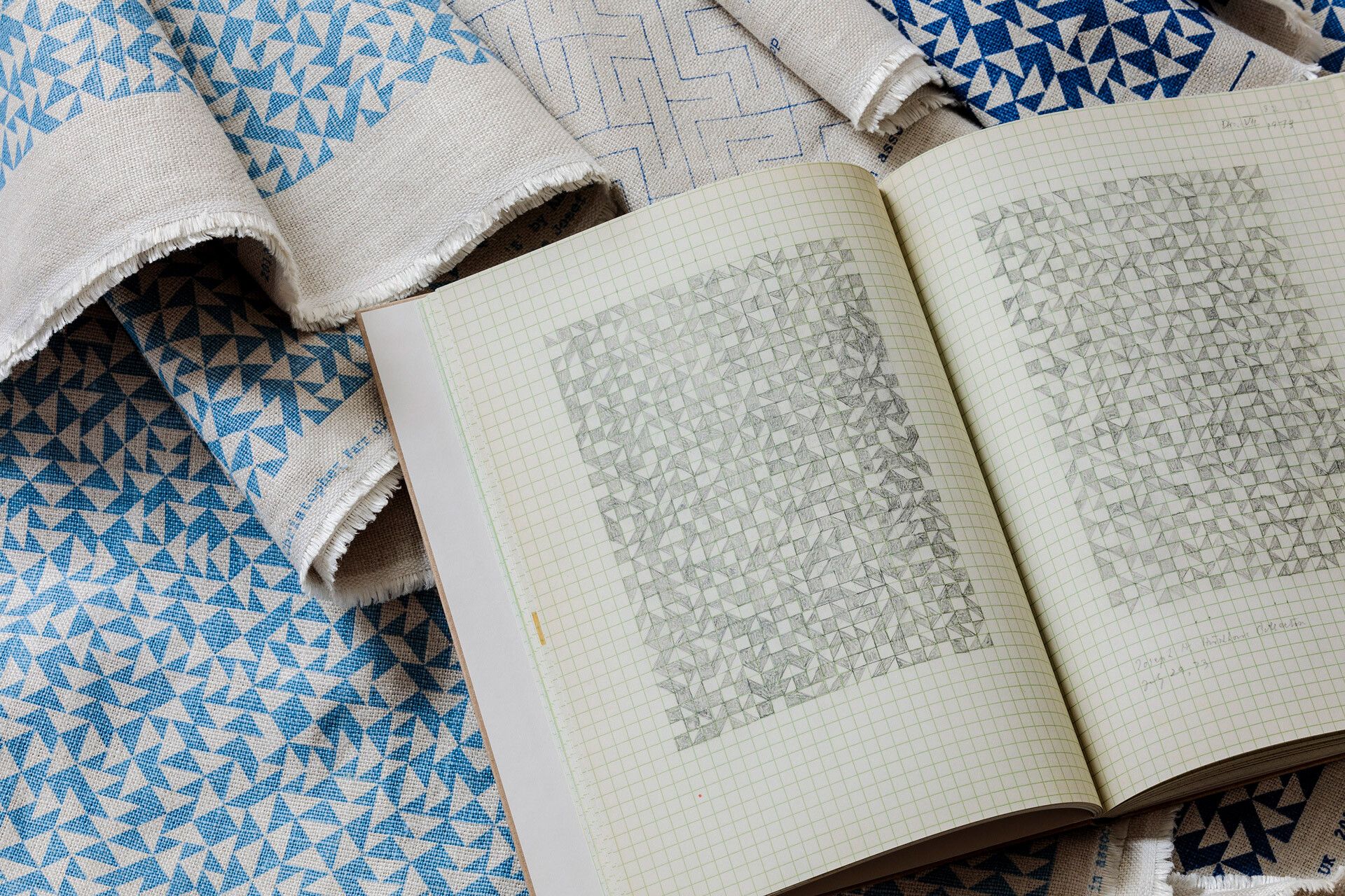 A photograph featuring textiles patterns and the book Notebook 1970–1980 by Anni Albers, dated 2019