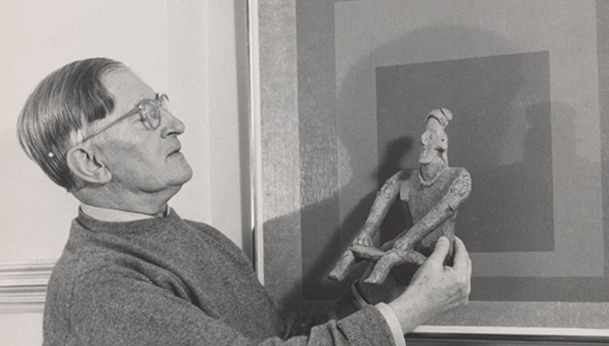 A photo by Lee Boltin, Untitled (Josef Albers Holding West Mexican Figure in front of Homage to the Square: Auriferous), 1958.© Lee Boltin. Photo courtesy of the Josef and Anni Albers Foundation.