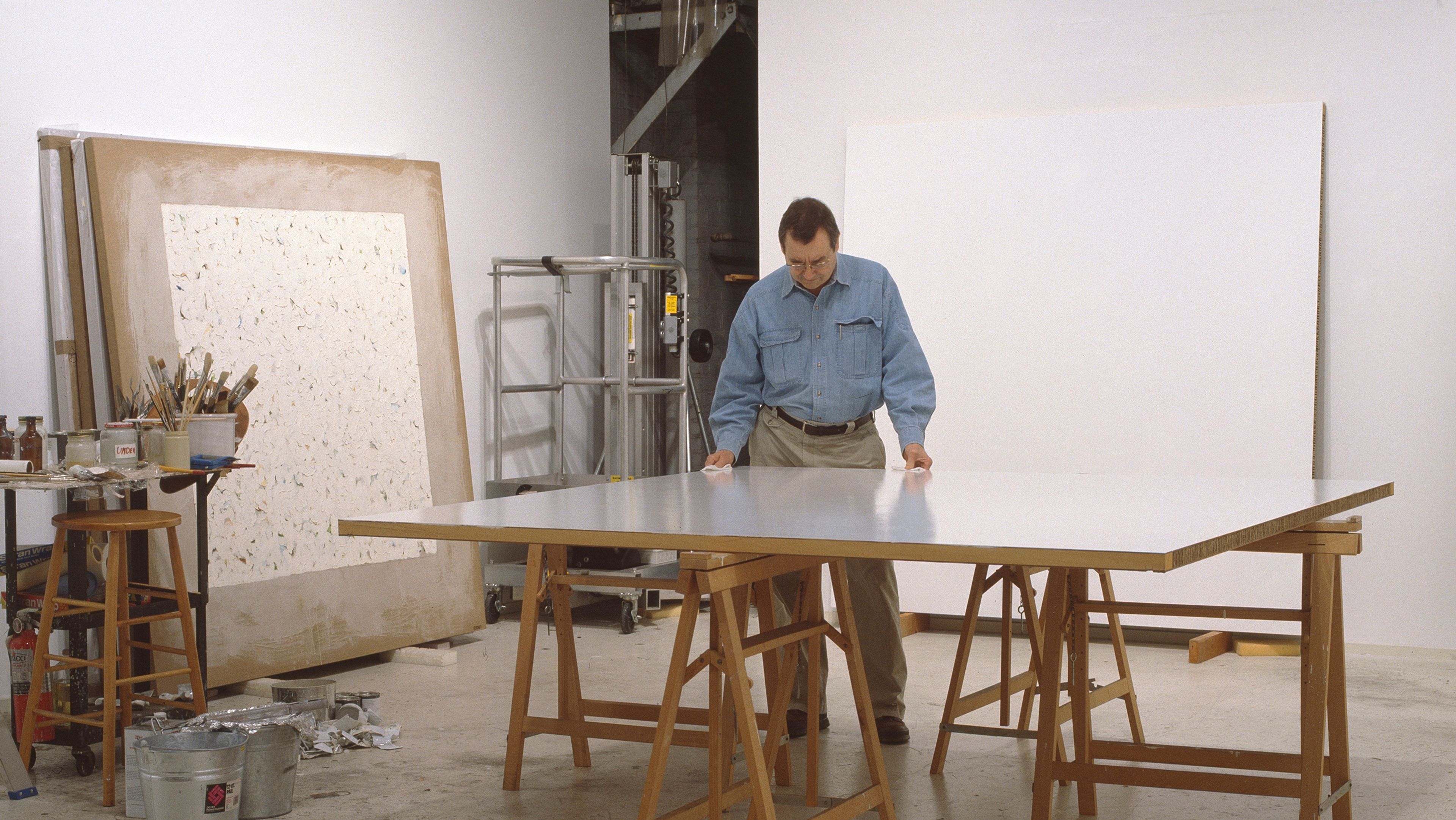 A color photograph of Robert Ryman in his studio, dated late 1990s.