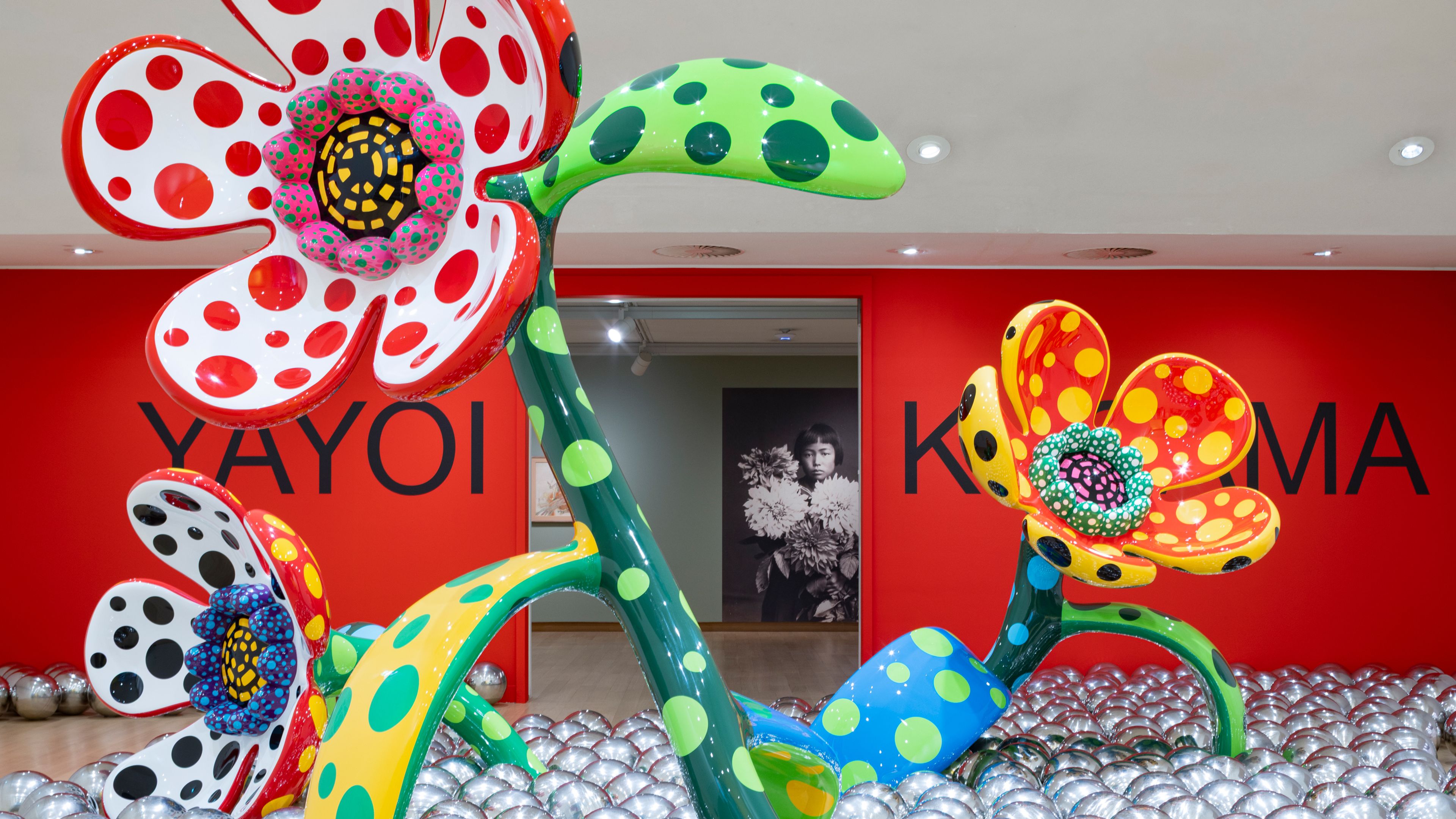 Installation view of Yayoi Kusama’s exhibition at the Stedelijk Museum Amsterdam, featuring monumental polka-dot flower sculptures.