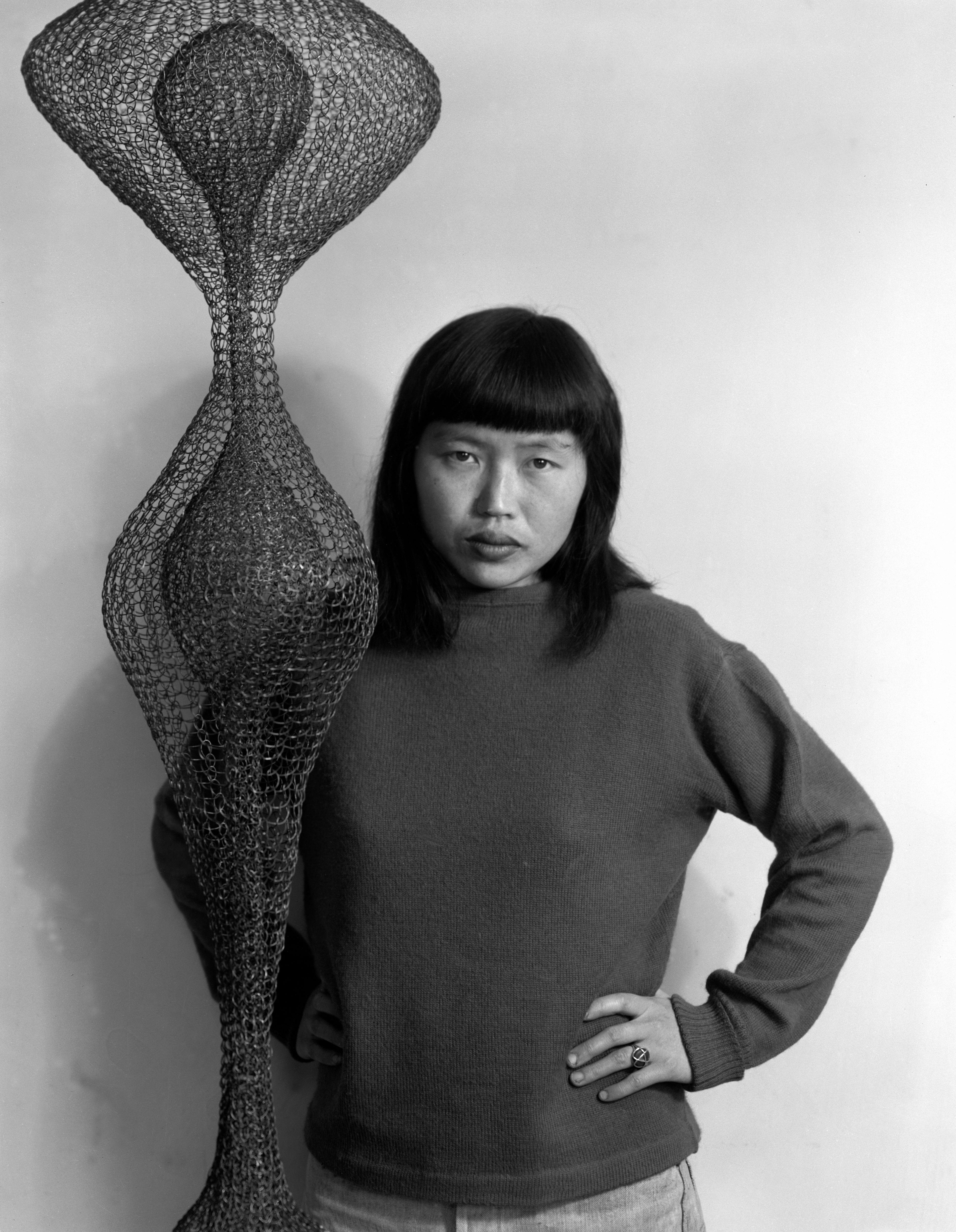 A black and white photograph by Imogen Cunningham of Ruth Asawa with hanging wire sculpture, dated 1951.