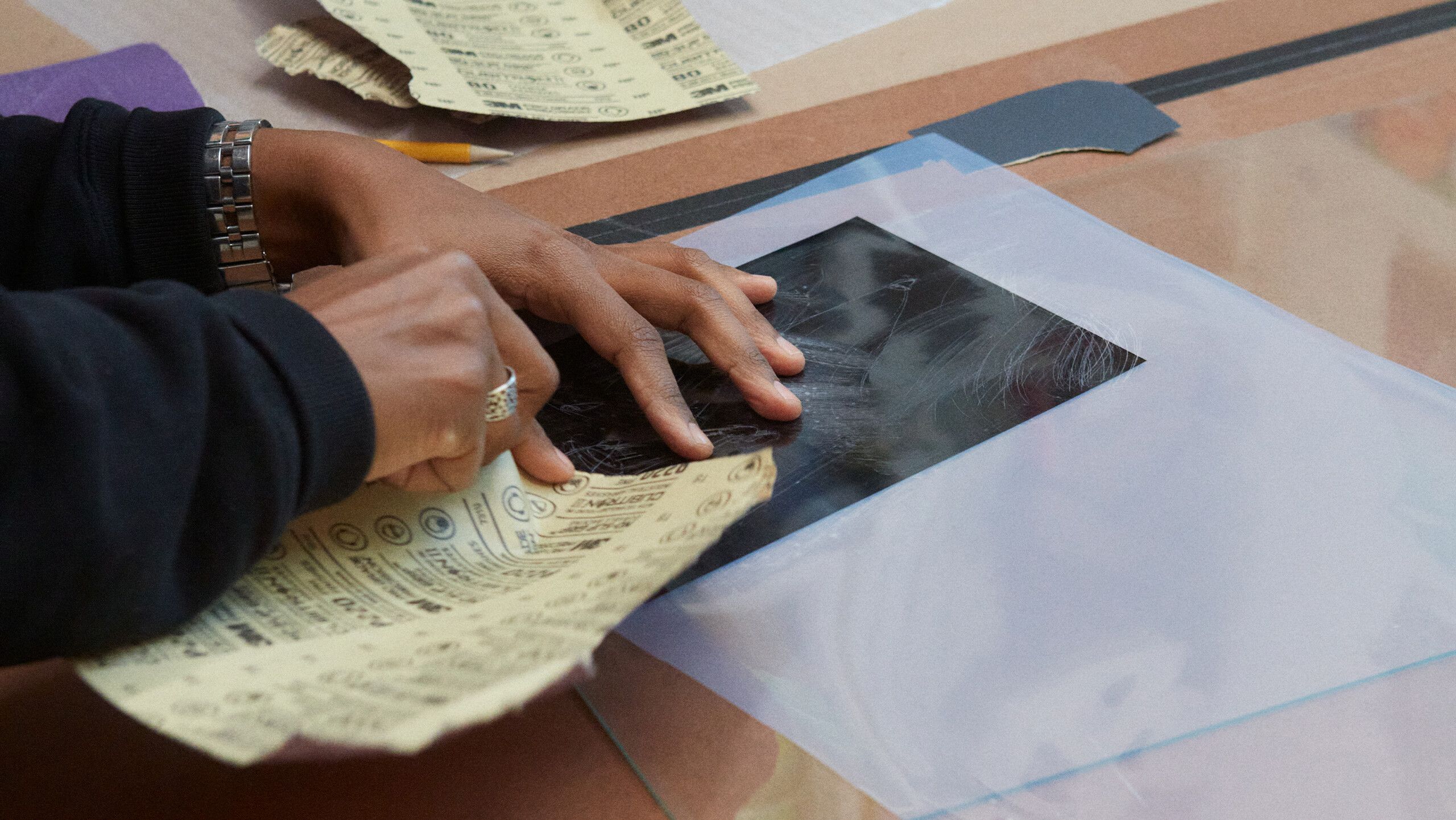 A photograph of Gale using sandpaper to mark a film, from which Diuguid will create the screen for their print, by Rafael Rios, dated 2022.