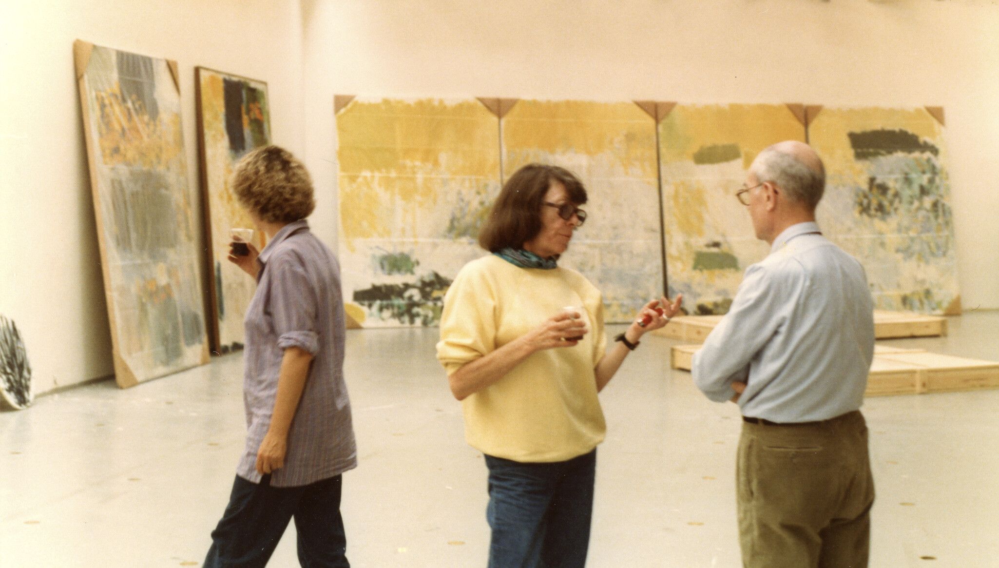 A photo of Joan Mitchell, Jean Fournier, and an unidentified person at the installation of Joan Mitchell: Choix de peintures, 1970–1982 at the Musée d'Art Moderne de la Ville de Paris, dated 1982.
