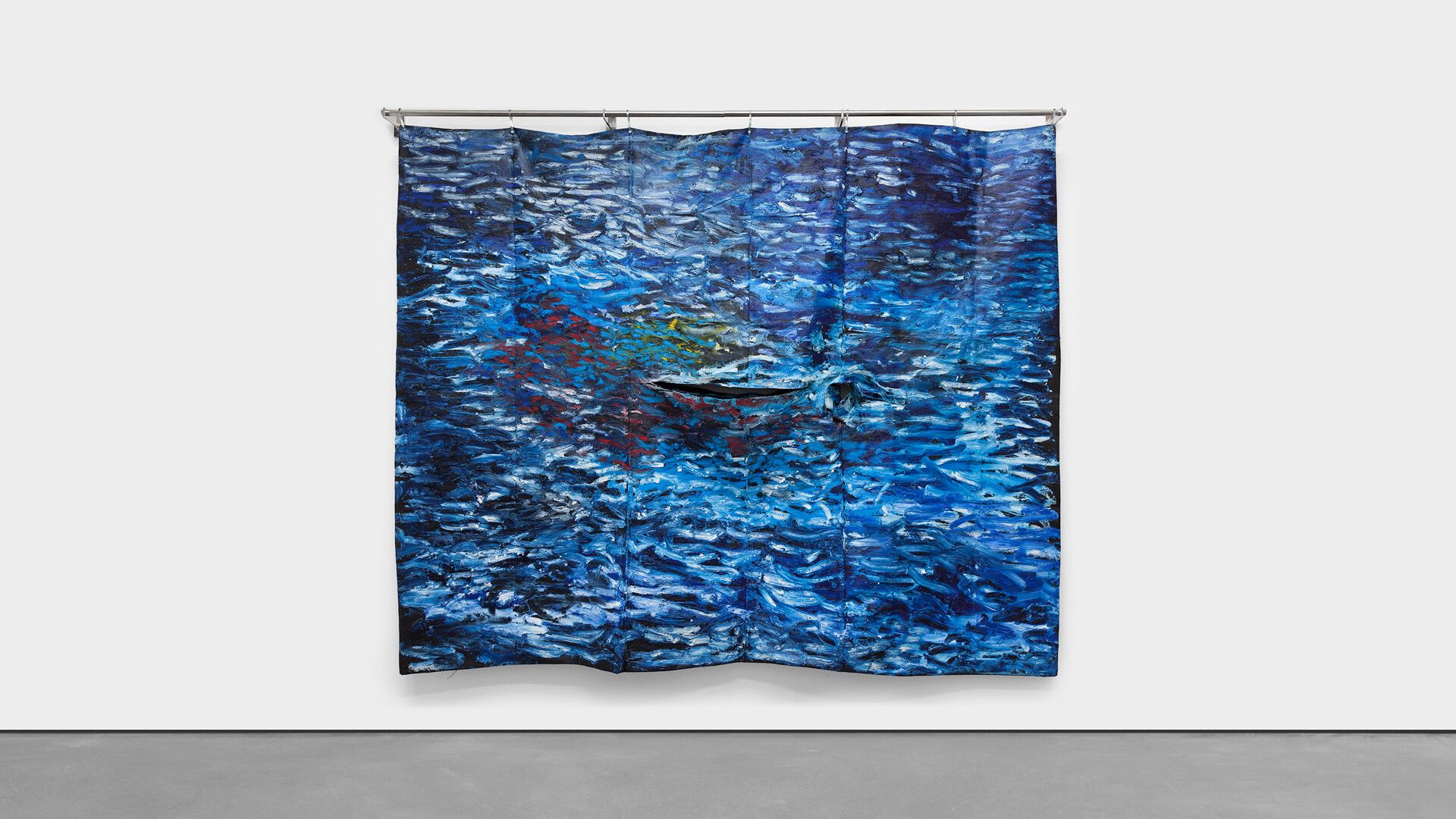 An installation view of an oil stick on velvet and linen, grommets and stainless steel rail wall-hanging work by Oscar Murillo, titled, surge (social cataracts), dated 2019.