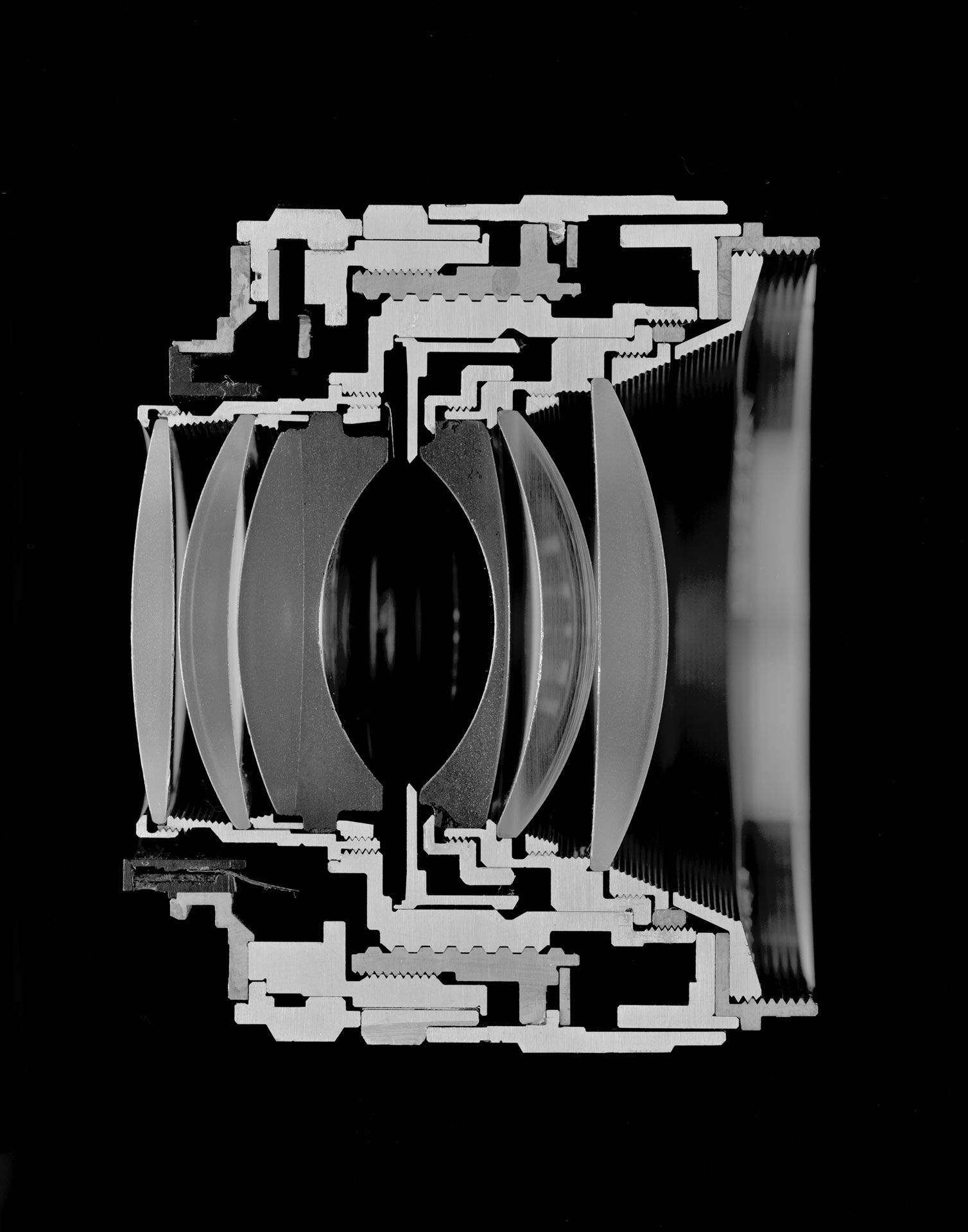 A black and white image of a camera lens sliced in half. Photograph by Christopher Williams, dated 2016.