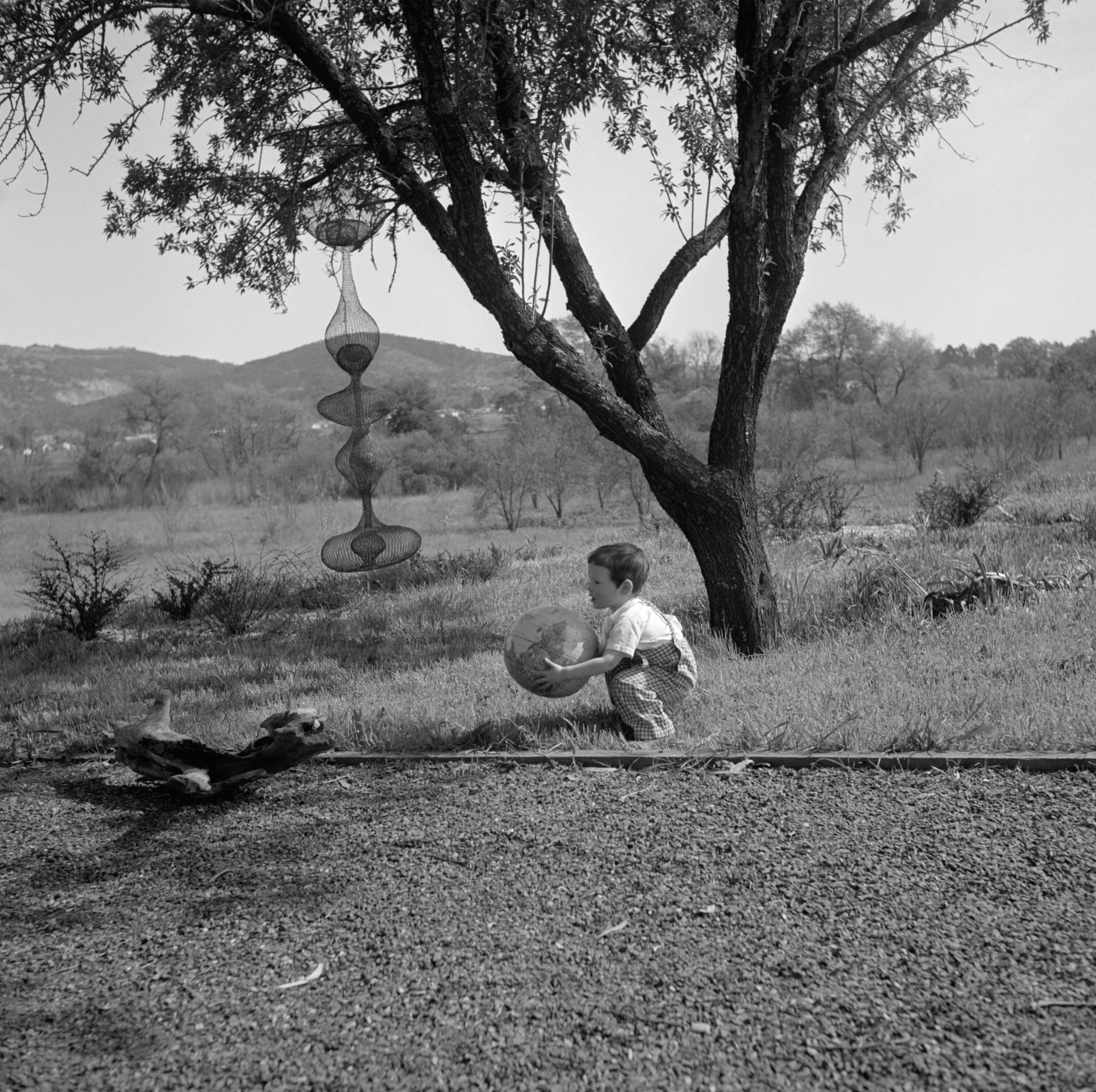 Xavier Lanier crouching in front of a hanging Ruth Asawa sculpture, 1953