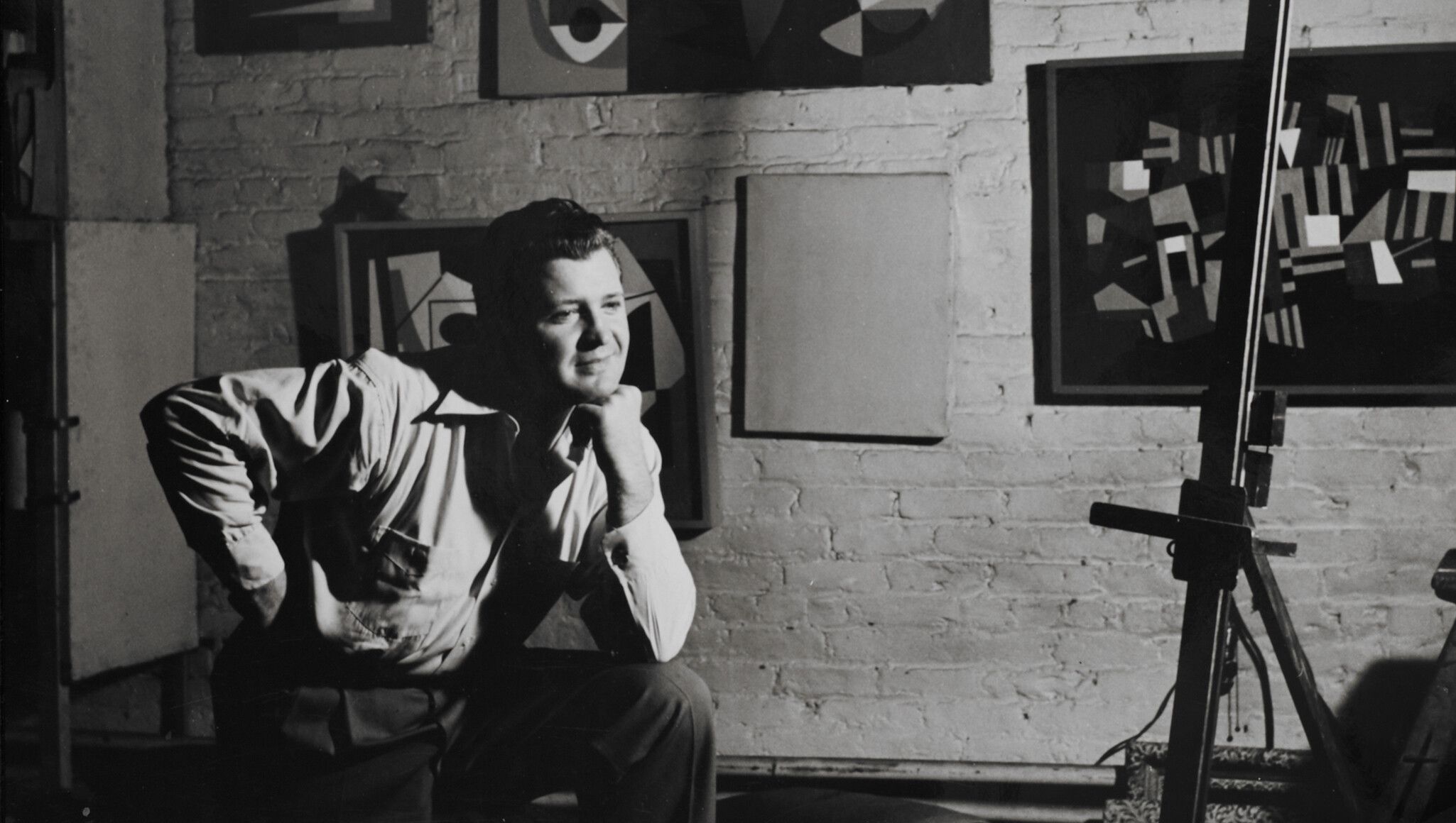 Ad Reinhardt in his studio sitting in front of his paintings in 1941-1942.