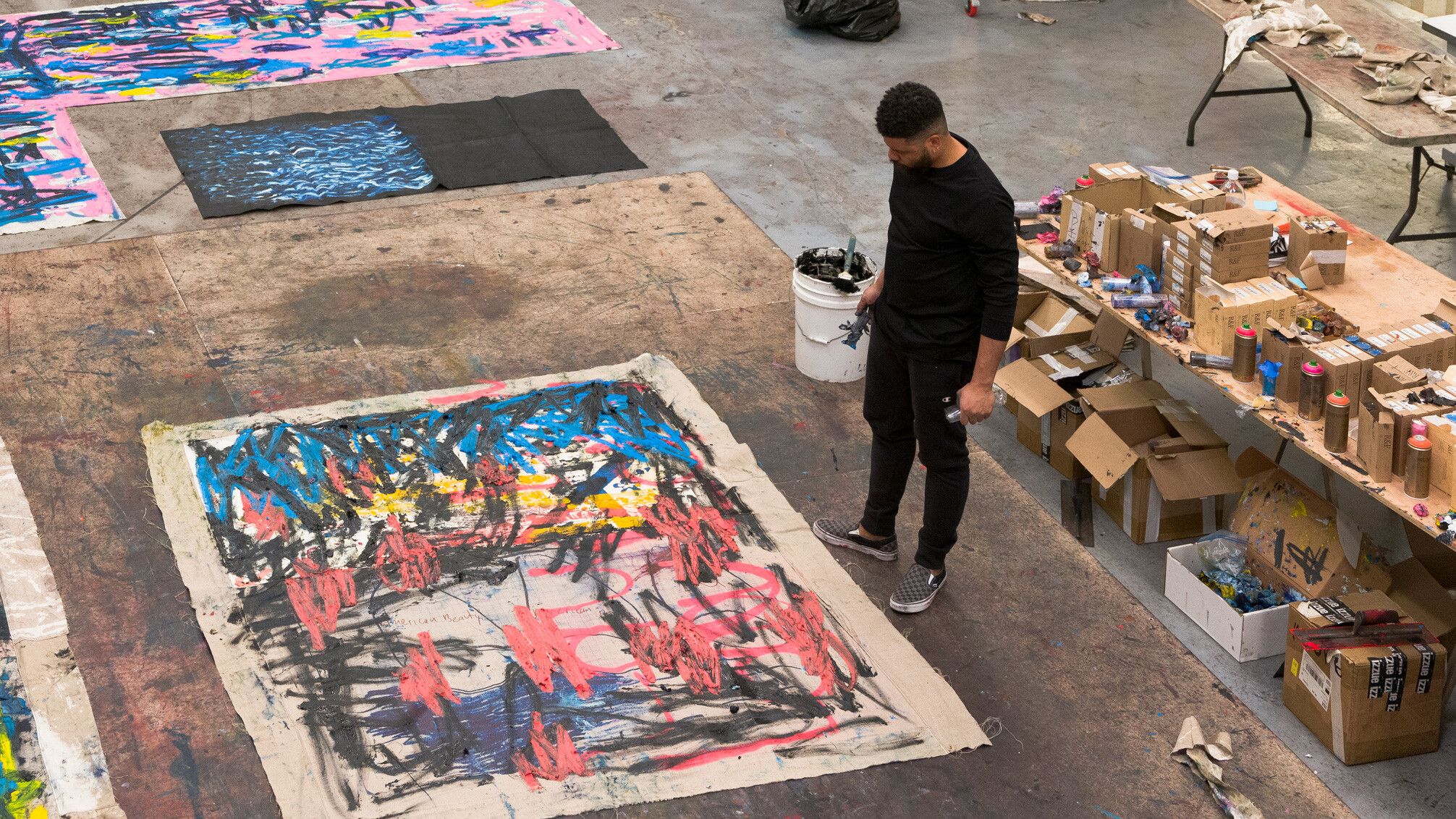 A photograph of Oscar Murillo in his studio with in-progress paintings from his surge series, dated 2022. Photo by Tim Bowditch