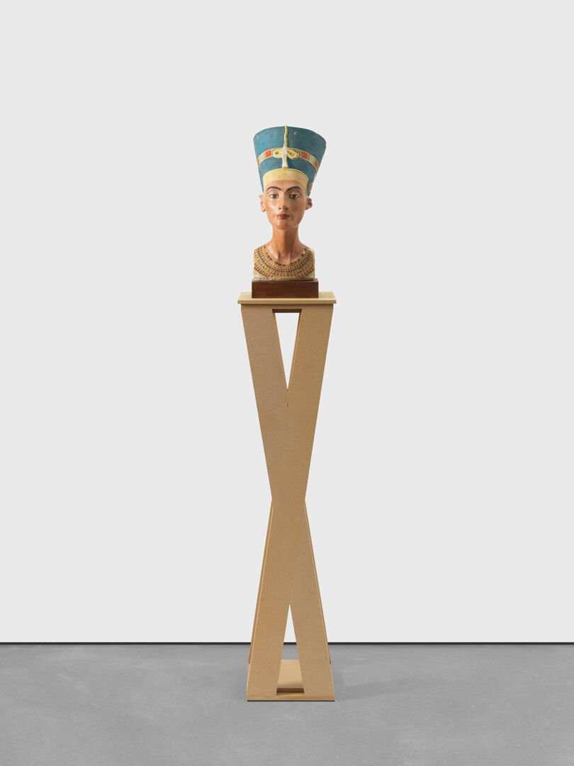 A plaster bust on wooden base, MDF plinth, postcard, sticker, and felt pen sculpture by Isa Genzken, titled Nefertiti, dated 2018.