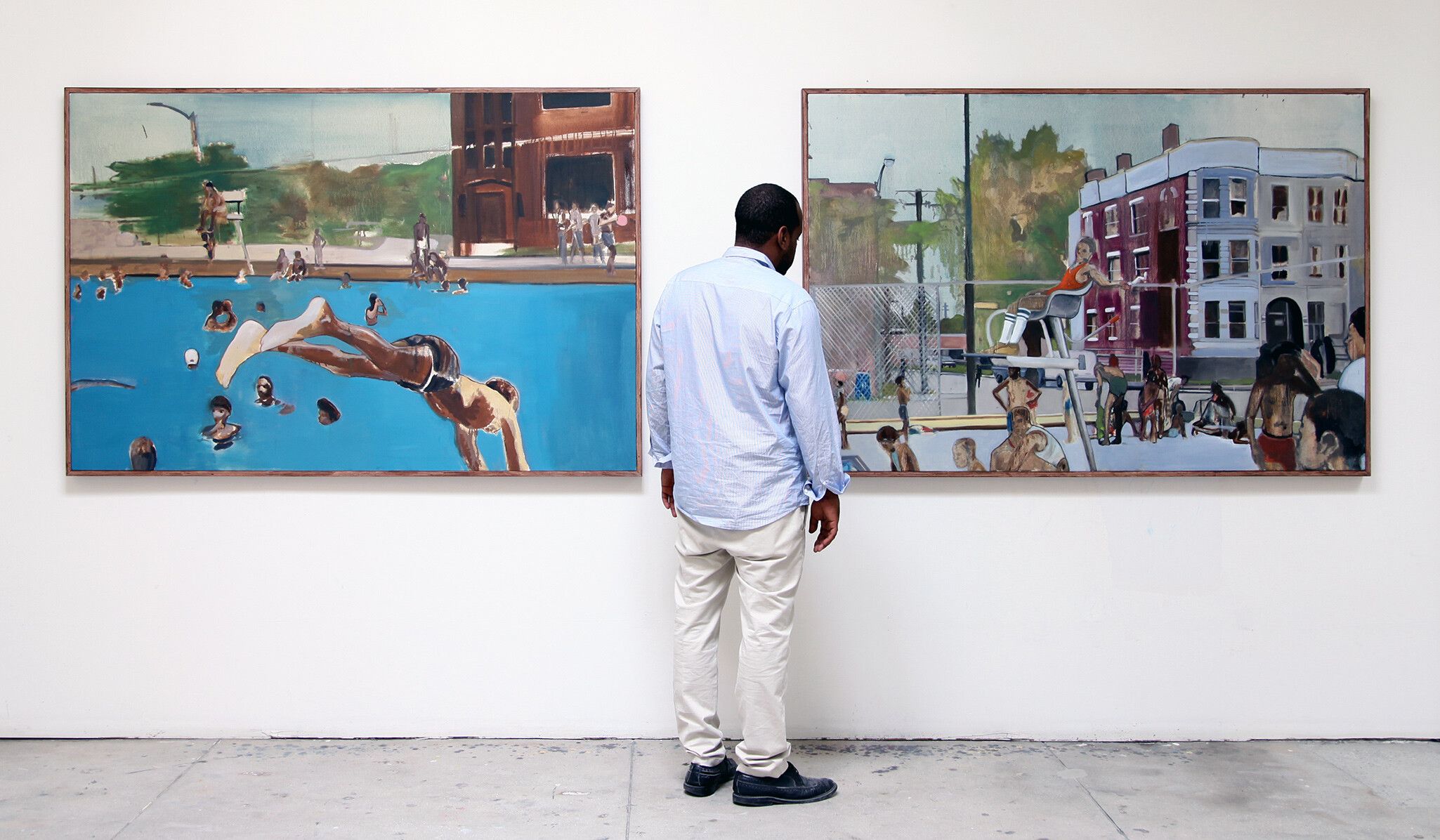 an installation view of two paintings by Noah Davis with the artist standing in front of them.