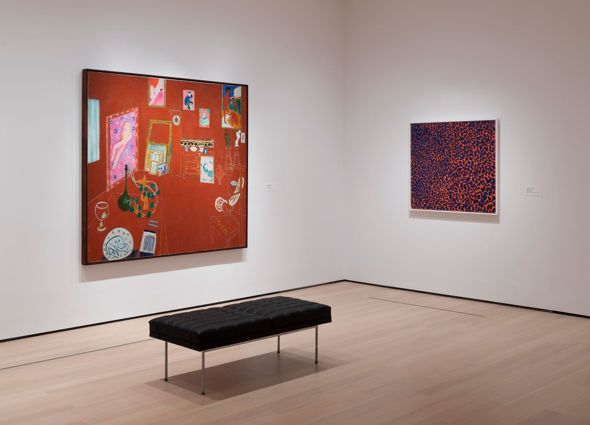 An Installation view of Henri Matisse at the Museum of Modern Art, New York, dated 2019. From left: Henri Matisse, The Red Studio, 1911; Alma Thomas, Fiery Sunset, 1973