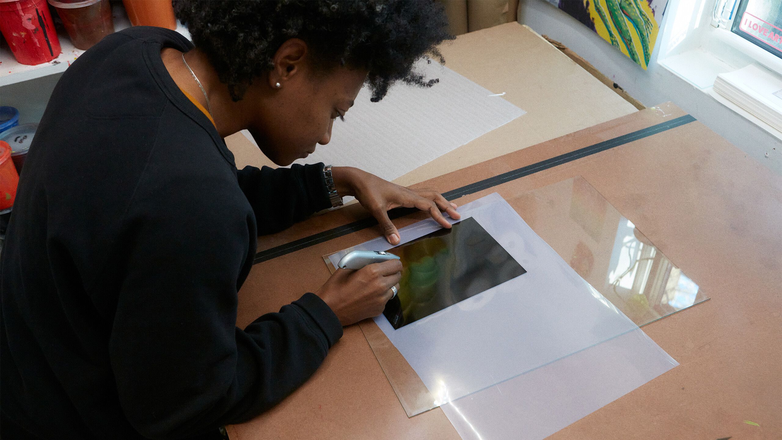 A photograph of Gale using a box cutter to scratch away pigment from a film by Rafael Rios, dated 2022.