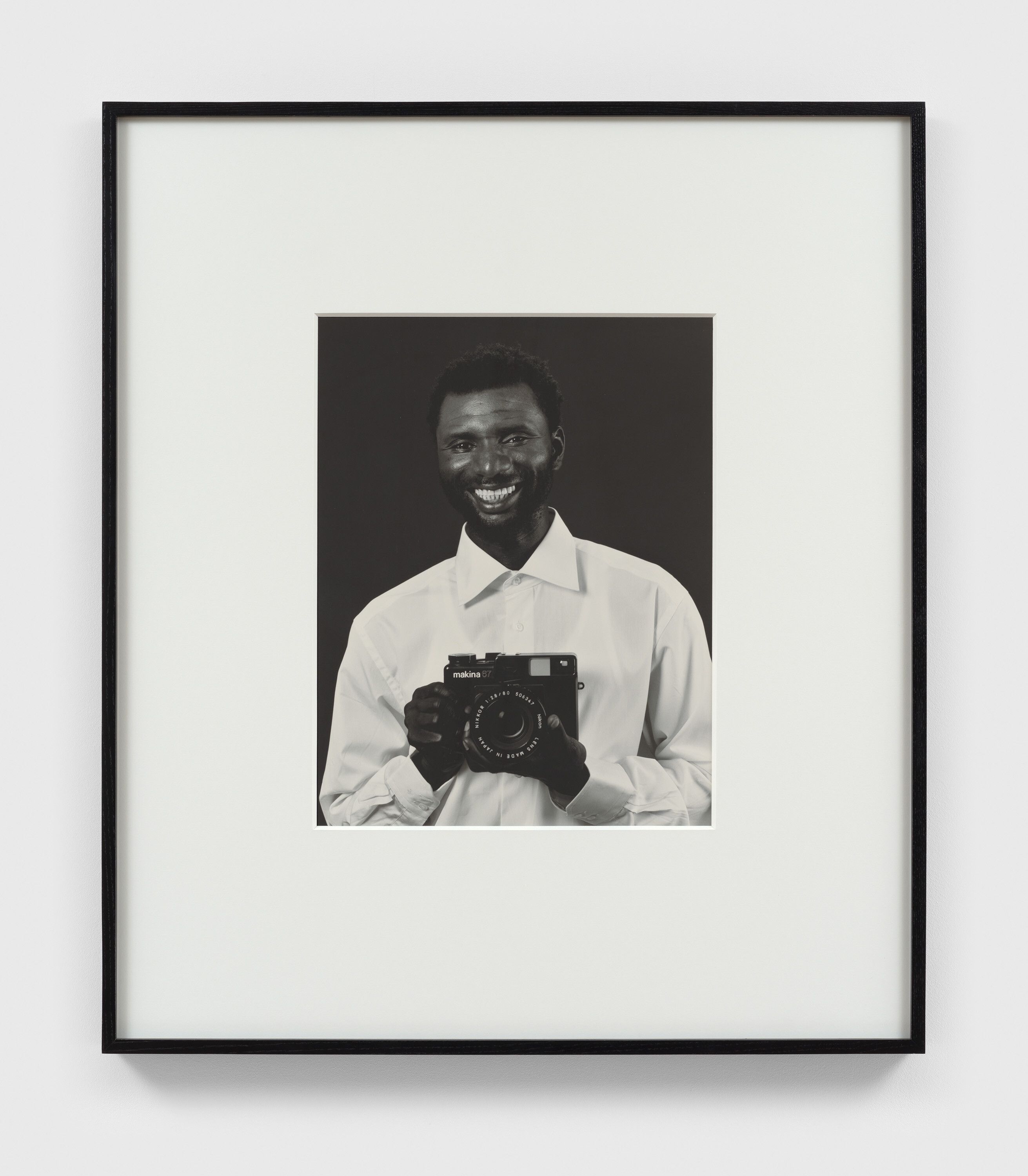 A photograph by Christopher Williams, titled Mustafa Kinte (Gambia) Camera: Makina 67 506347 Plaubel Feinmechanik und Optik GmbH Borsigallee 37 60388 Frankfurt am Main, Germany Shirt: Van Laack Shirt Kent 64 41061 Mönchengladbach, Germany Dirk Schaper Studio, Berlin July 20, 2007, dated 2008.