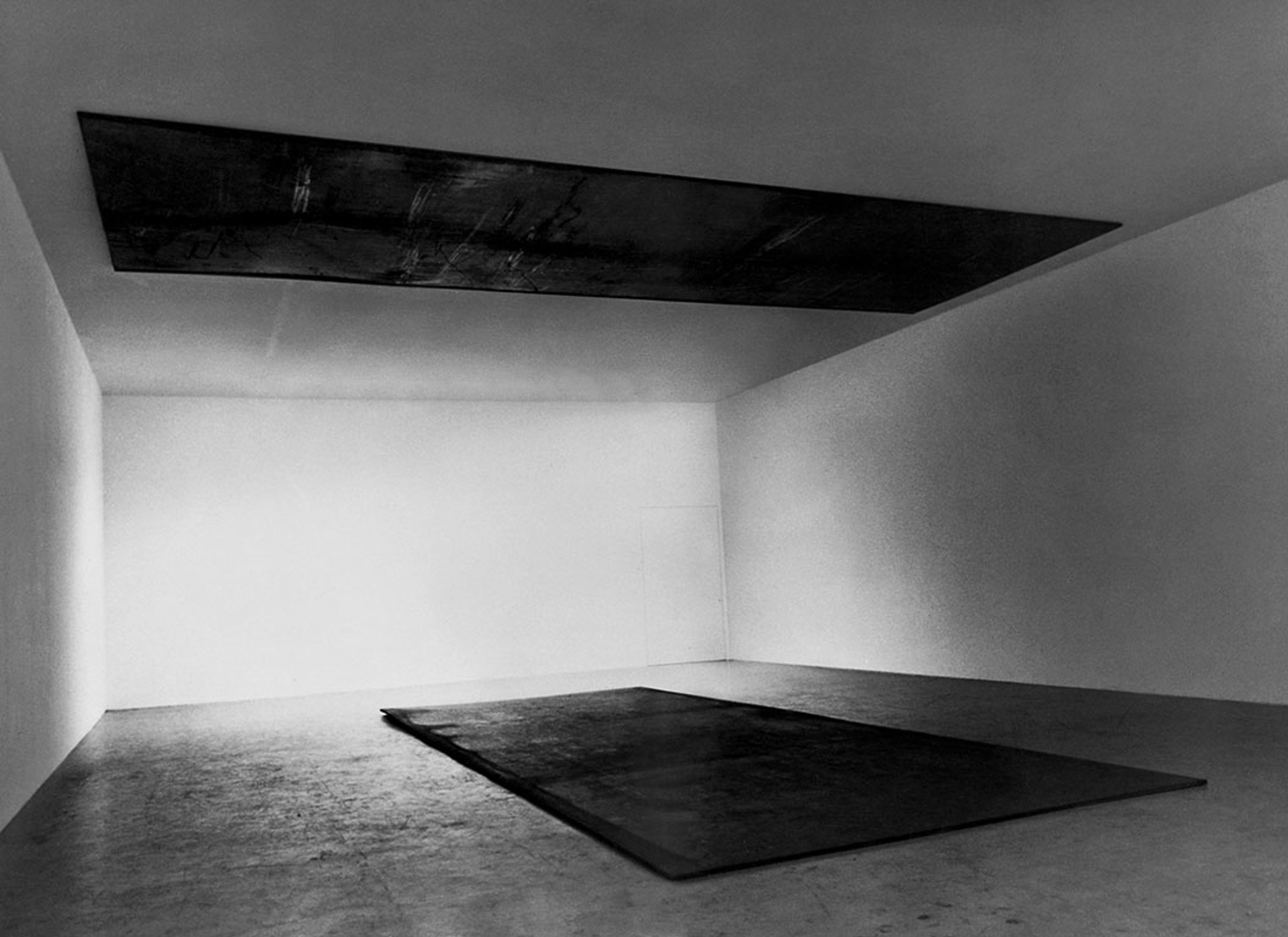 A hot-rolled steel sculpture made of two plates parallel to each other on the ceiling and floor by Richard Serra titled Delineator, dated 1974-75.