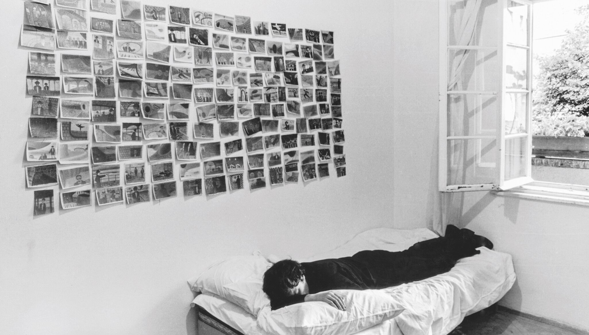 A photo of Franz West in front of a wall of his early drawings, dated 1973