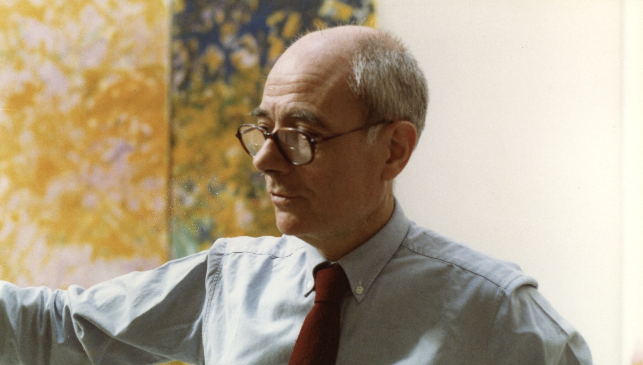 A photo of Jean Fournier standing in front of Chez ma soeur during the installation of Joan Mitchell: Choix de peintures, 1970–1982 at the Musée d'Art Moderne de la Ville de Paris, dated 1982