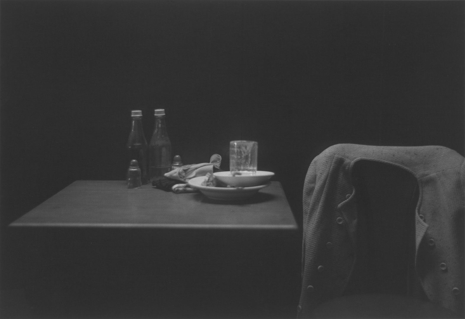A photograph by Roy DeCarava, titled Catsup bottles, table and coat, dated 1952.