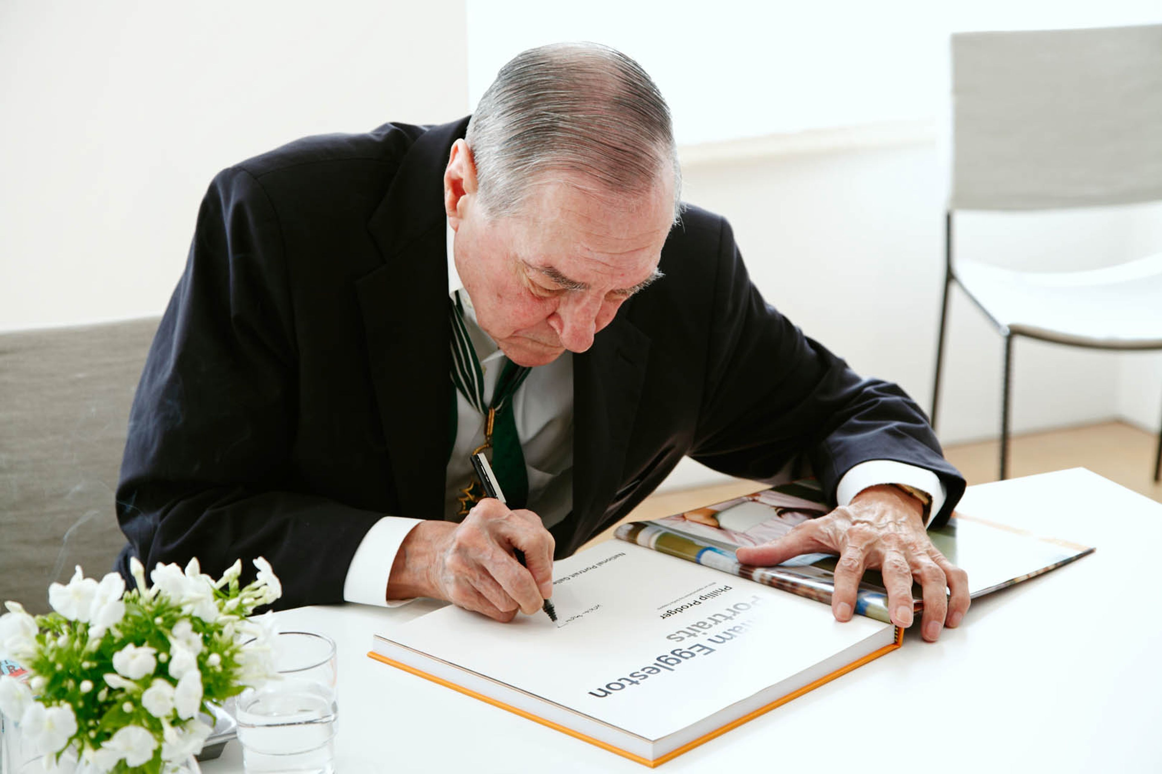 A photograph of William Eggleston signing books at David Zwirner in London, dated 2016.