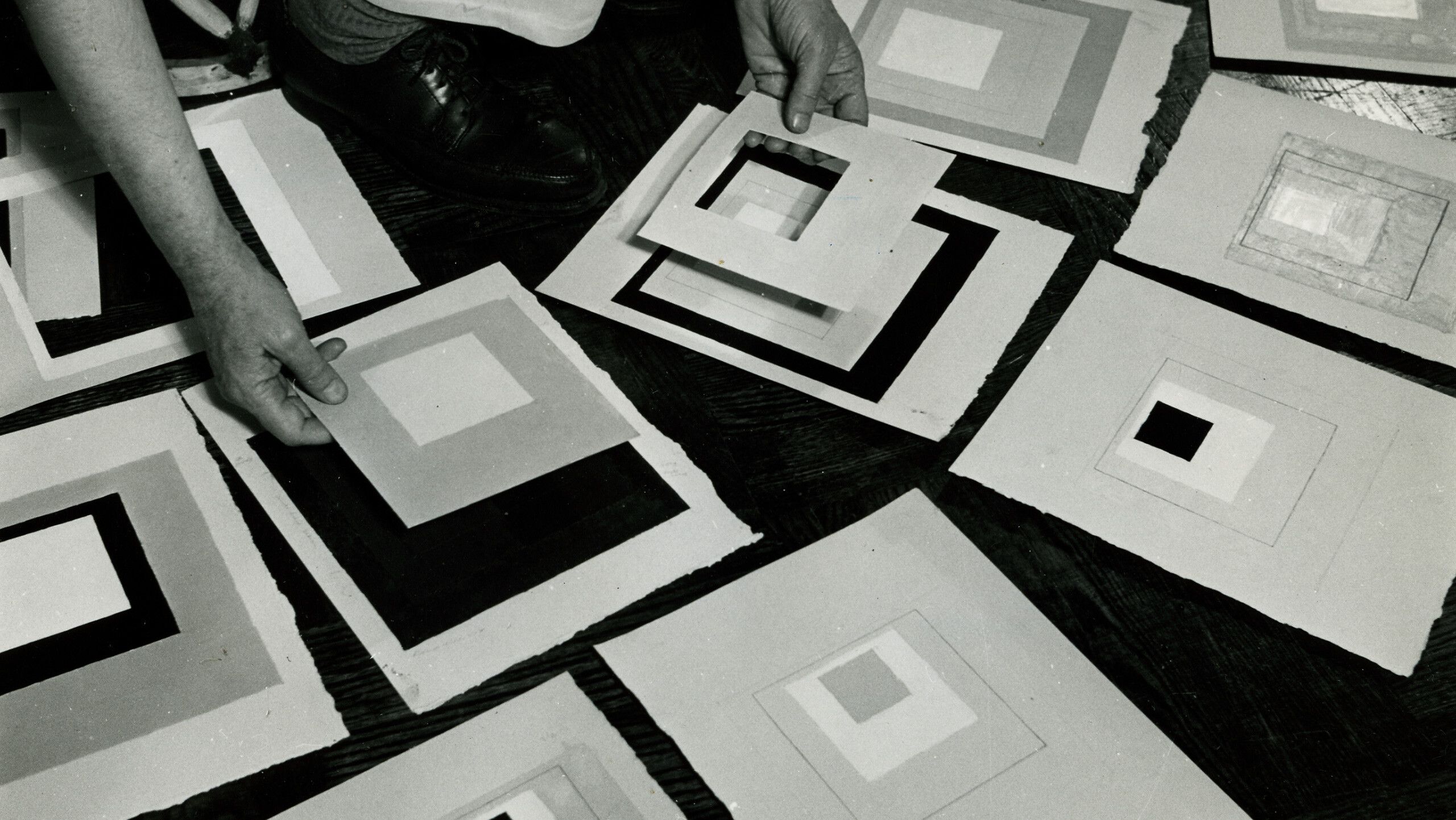 A photo of Josef Albers reviewing his artwork taken by Rudy Burckhardt