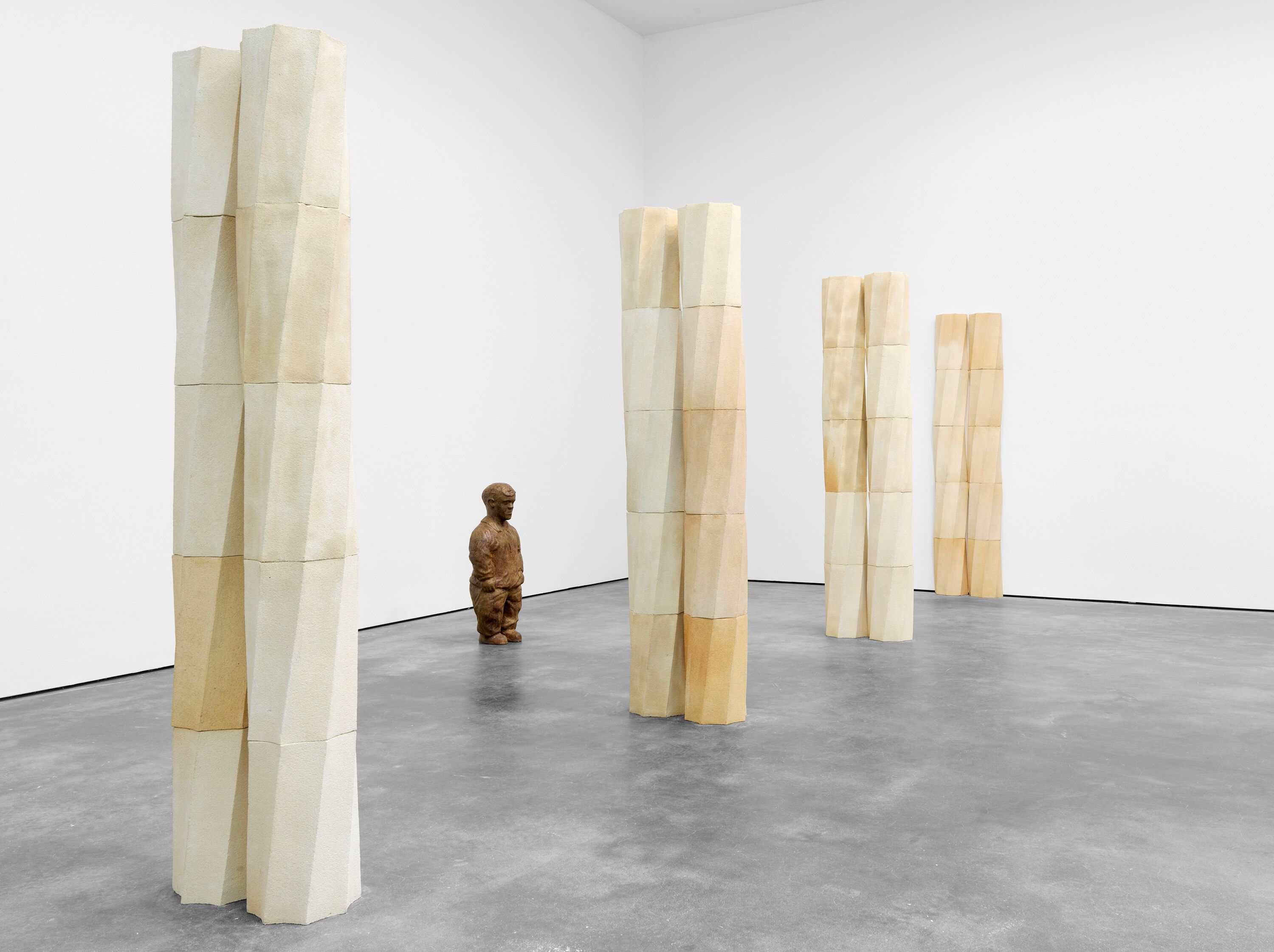 An installation of terracotta columns and a bronze figure by Juan Muñoz, titled Schwelle (Threshold), dated 1991.