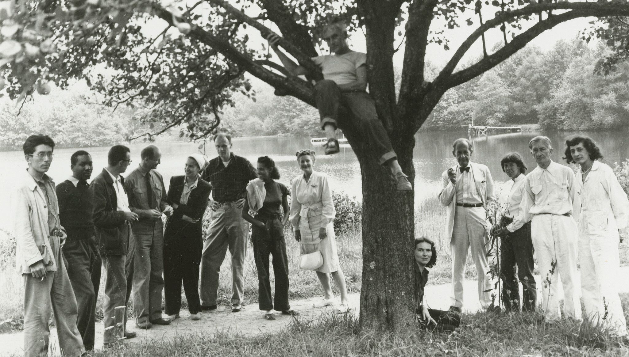 A photo of the Summer Arts Institute Faculty, at Black Mountain College, dated 1946. Left to right: Leo Amino, Jacob Lawrence, Leo Lionni, Ted Dreier, Nora Lionni, Beaumont Newhall, Gwendolyn Lawrence, Ise Gropius, Jean Varda (in tree), Nancy Newhall (sitting), Walter Gropius, Mary “Molly” Gregory, Josef Albers, Anni Albers. 