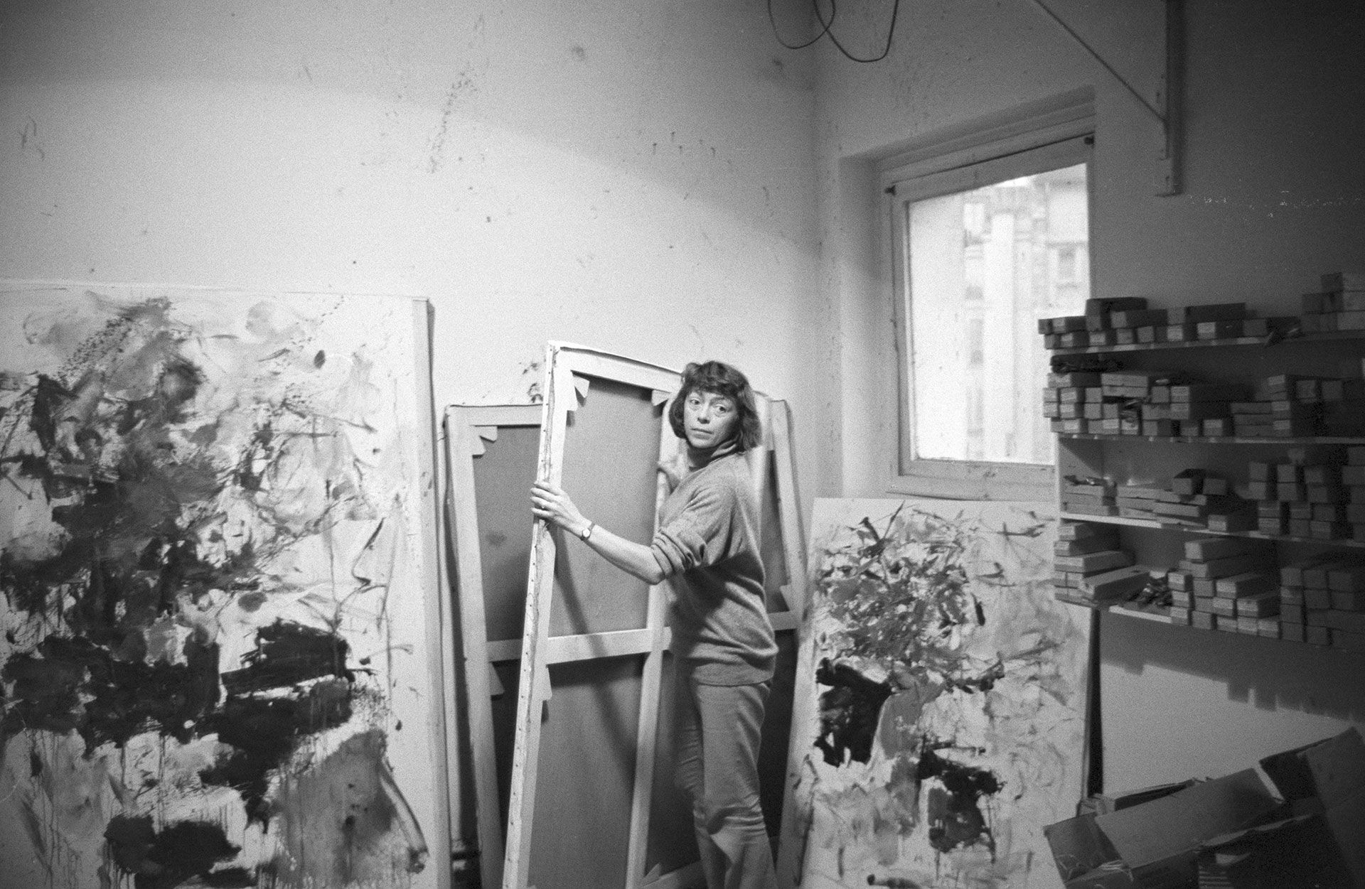 A photograph by jean-Pierre Biot of Joan Mitchell moving a canvas in her studio, dated 1962.