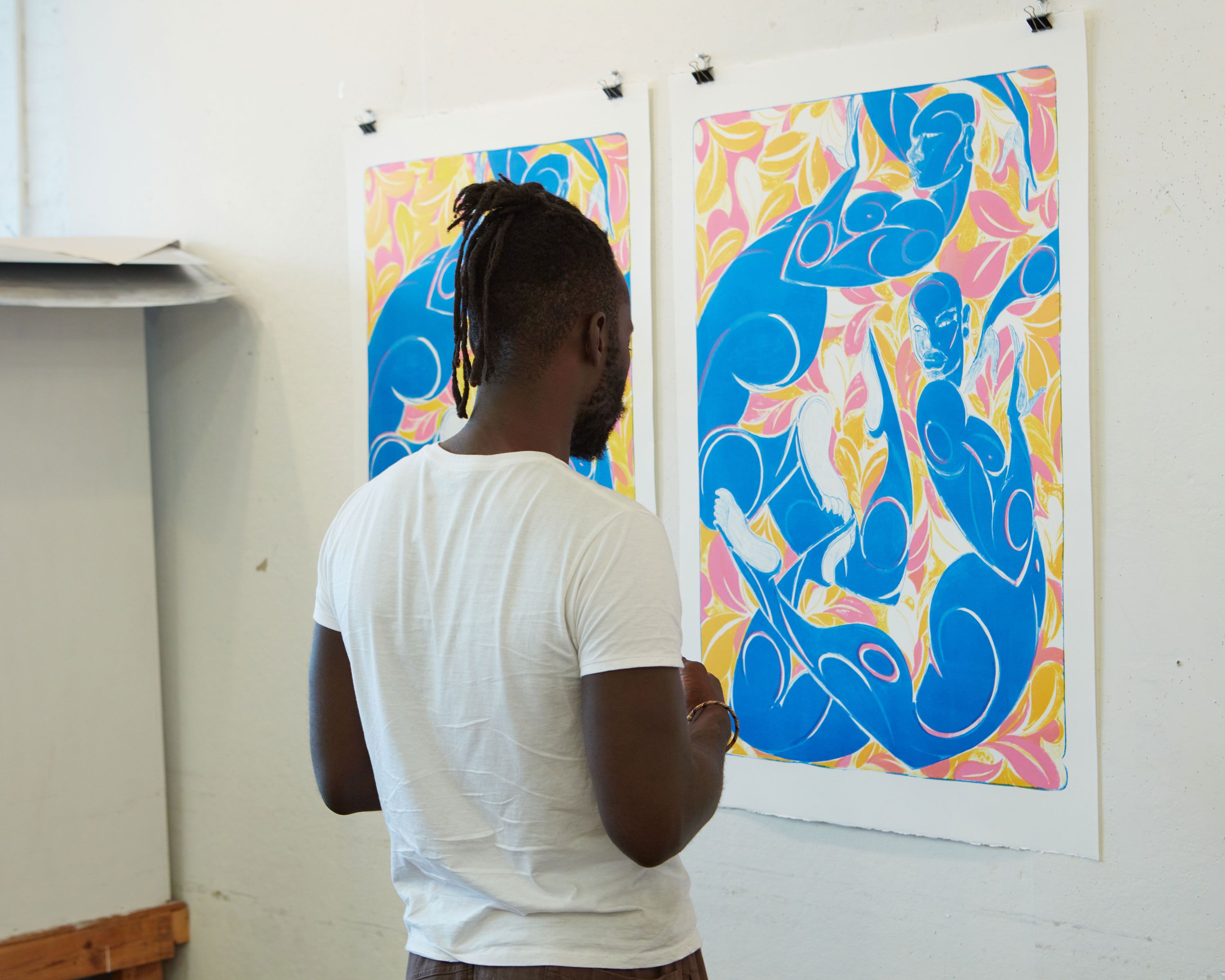 This photograph features Adeniyi-Jones standing in front of his first lithographs hung on the wall, dated 2022. Photo by Rafael Rios