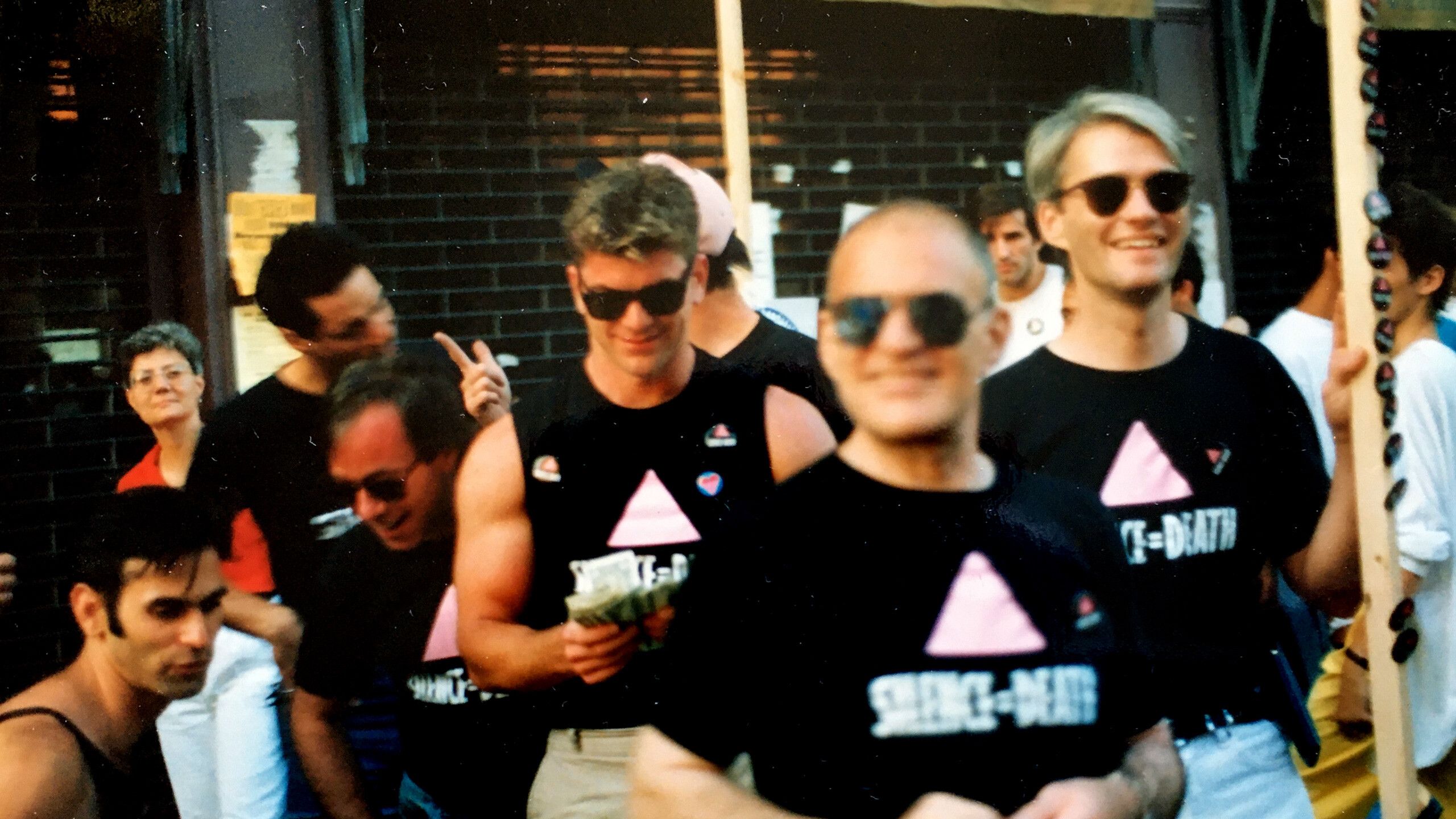A photo of Avram Finkelstein, Frank Jump, Jerry Smith, Steve Webb, Larry Kramer, and Barry Gingell wearing Silence=Death t-shirts in the Christopher Street Fair in New York for Pride in 1987. 