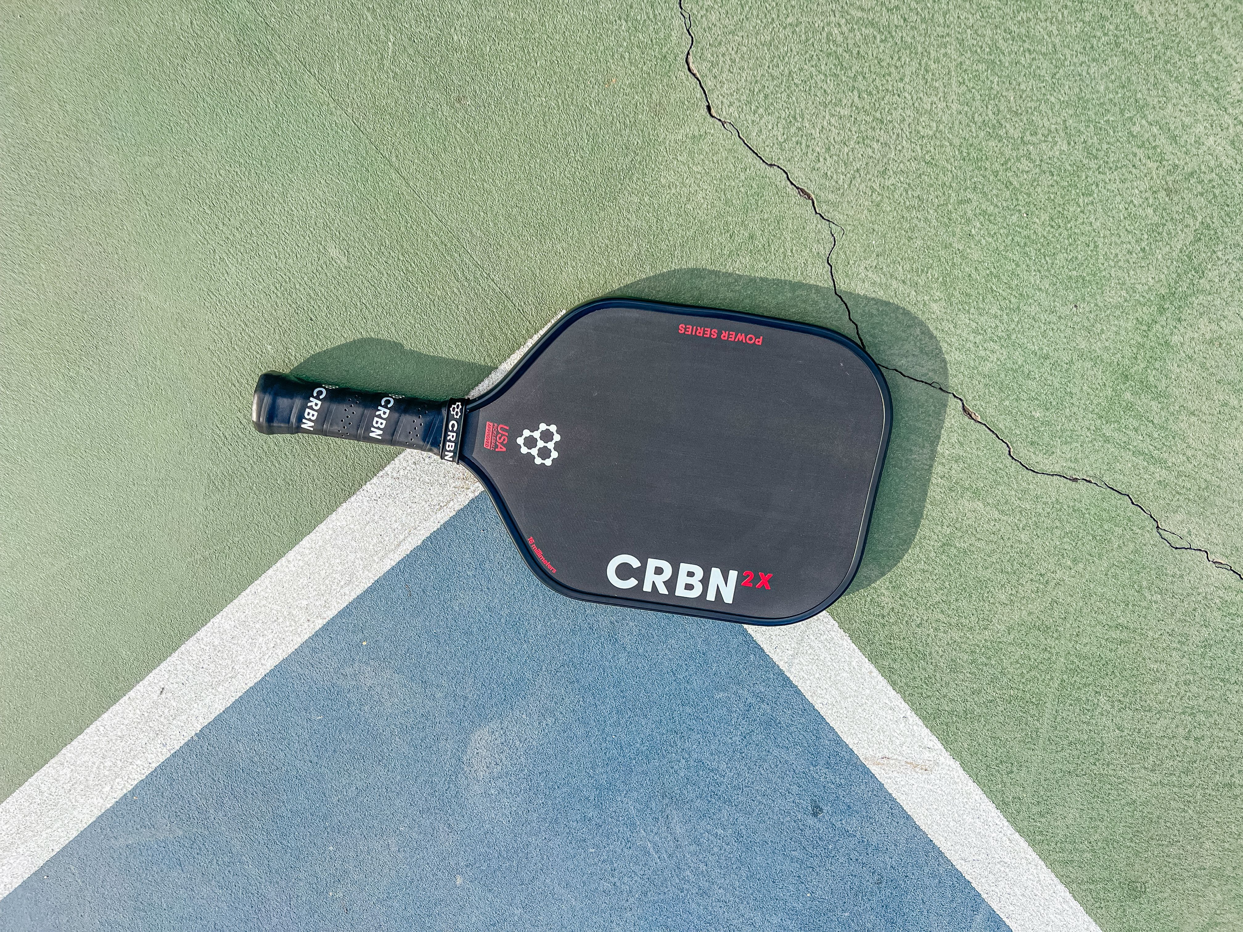 The CRBN-2X Power Series paddle placed on a pickleball court
