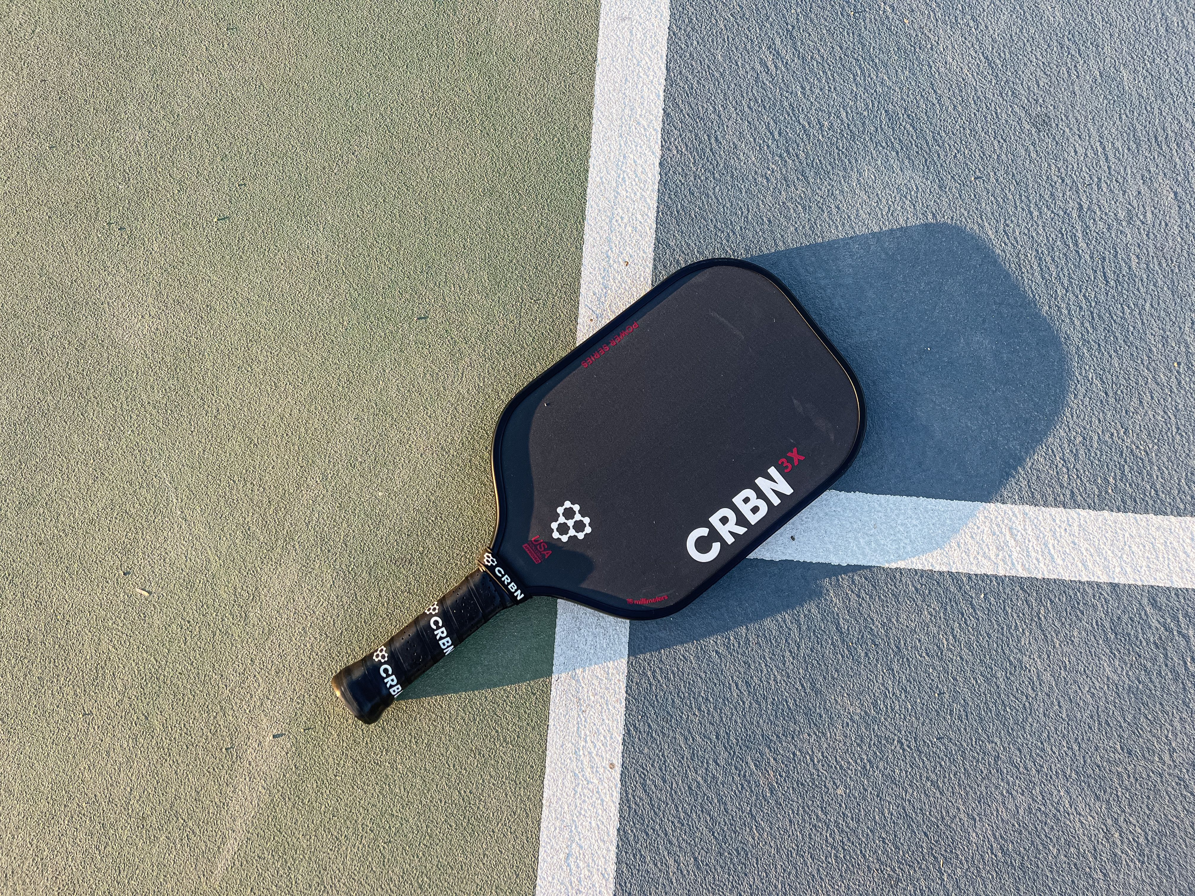 The CRBN-3X Power Series paddle resting on a pickleball court