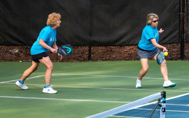 Pickleball players wearing team name shirts concentrating on a shot