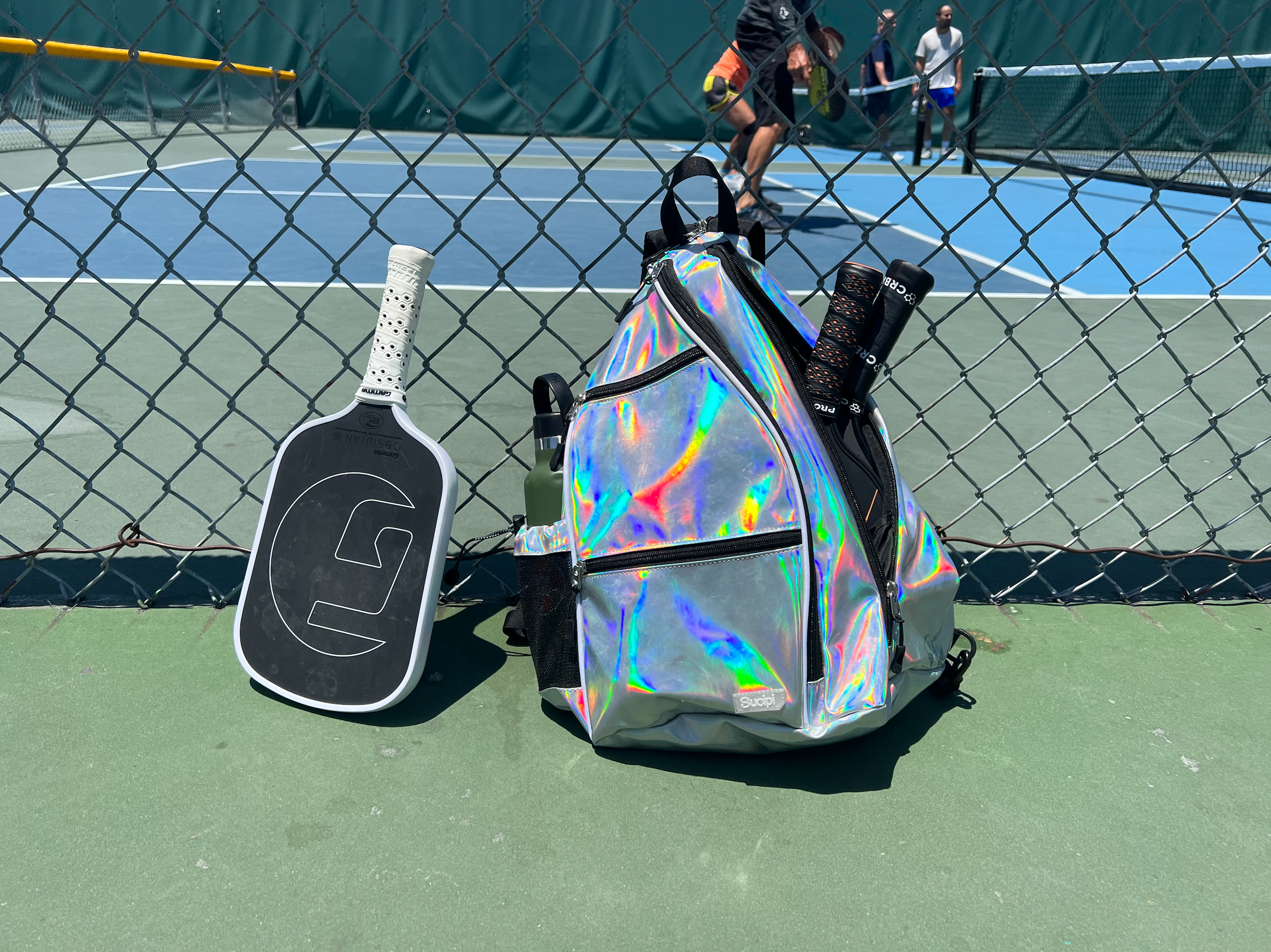 The Sucipi Pickleball Backpack holding several paddles on a pickleball court