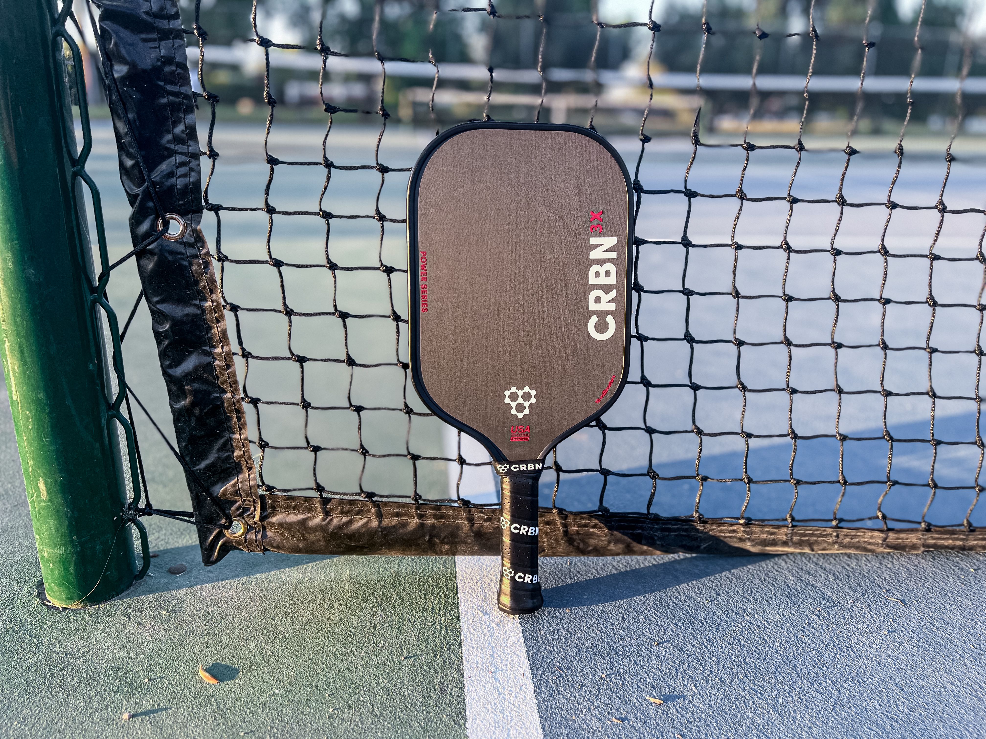 The CRBN-3X Power Series resting against a pickleball net