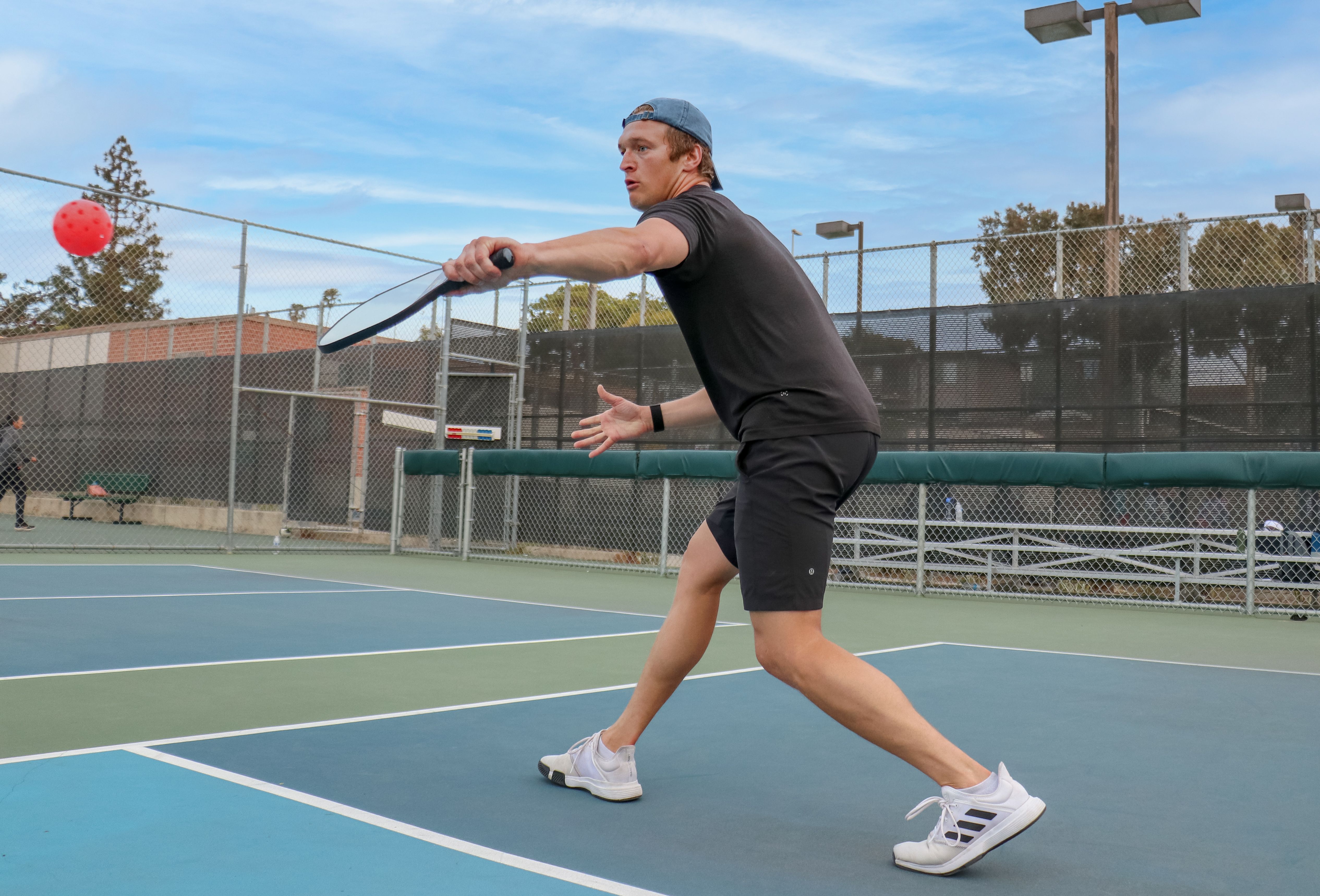 Player reaches across the pickleball court to hit a ball