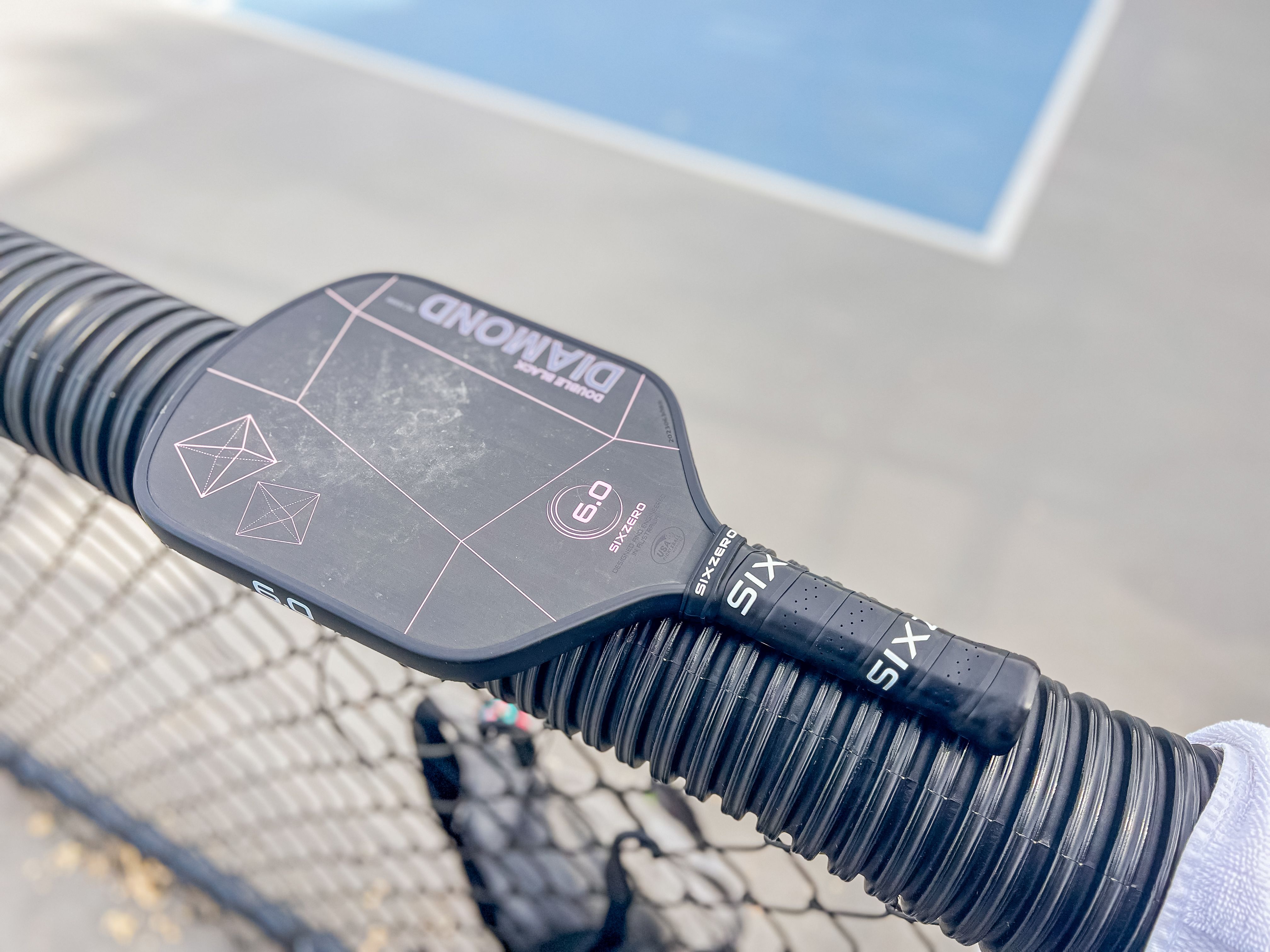 The Six Zero Double Black Diamond Control paddle resting at the side of a pickleball court