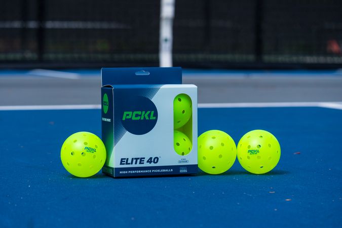 A box of PCKL Elite 40 pickleball balls placed on a court