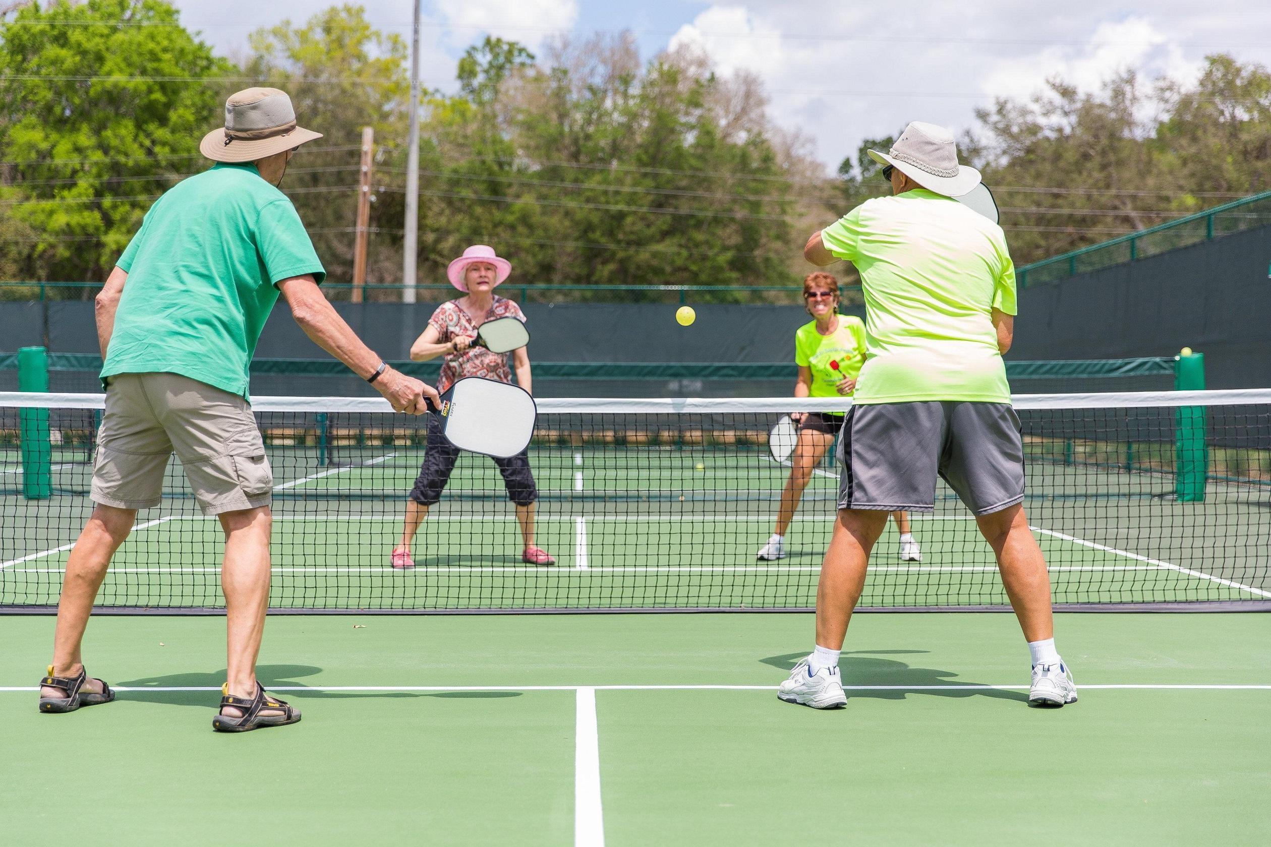 Four pickleball players in the middle of a pickleball game on a sunny day